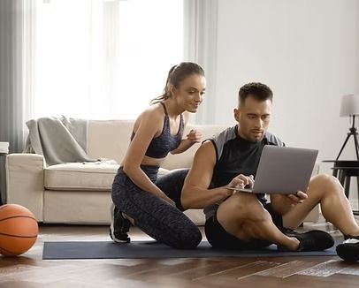 Woman and man in workout clothes on mat looking at laptop in living room.