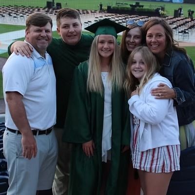 Family celebrates graduation at a stadium; woman in green cap, siblings, parents smiling.