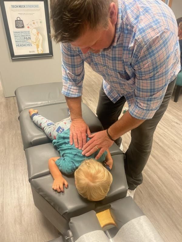 Chiropractor adjusting a young child on a treatment table. The child is lying face down.