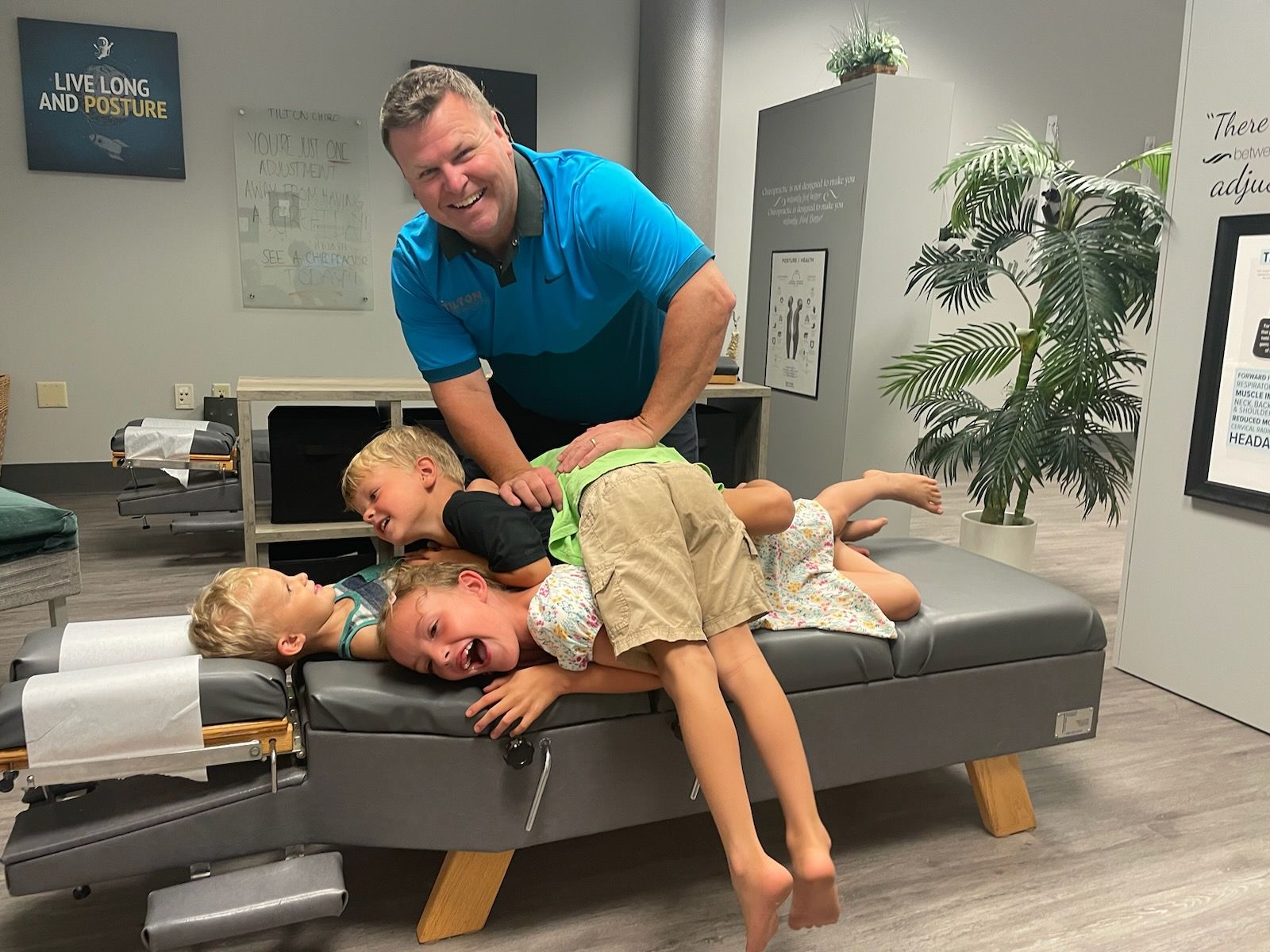 Chiropractor smiling, adjusting three children lying on an examination table. Interior, office setting.