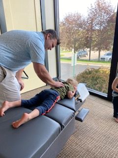 A person adjusting a child lying on a treatment table. Large window with a view in background.