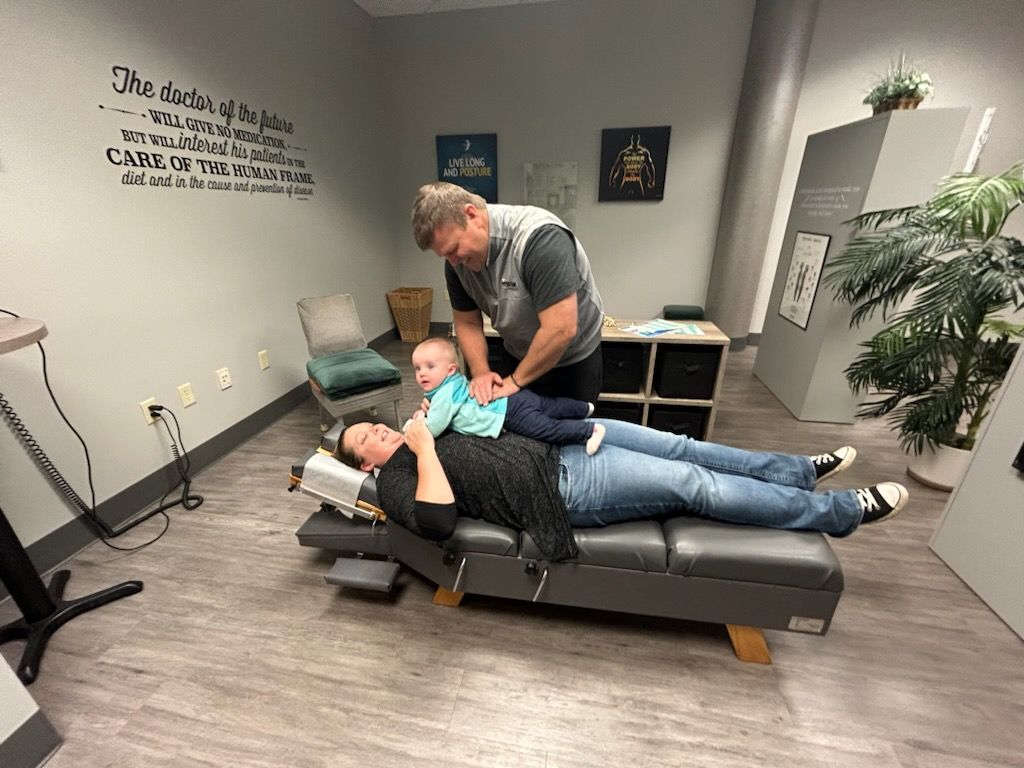Chiropractor adjusting a child on a mother lying on a therapy table in a clinic.