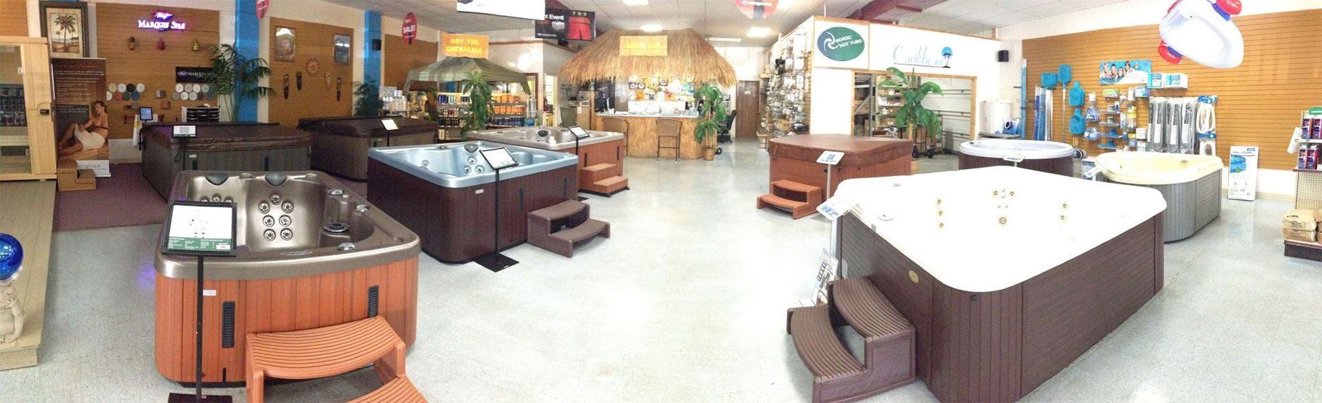 A showroom displaying multiple hot tubs of various shapes and sizes, indoors with wooden accents and signs.