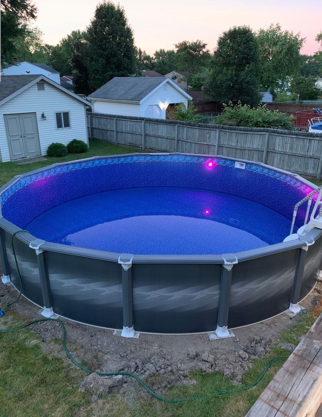 Above-ground pool with blue interior, surrounded by a dark frame, in a backyard setting.