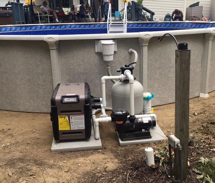 Pool pump and heater system next to an above-ground pool. Includes a sand filter and plumbing.
