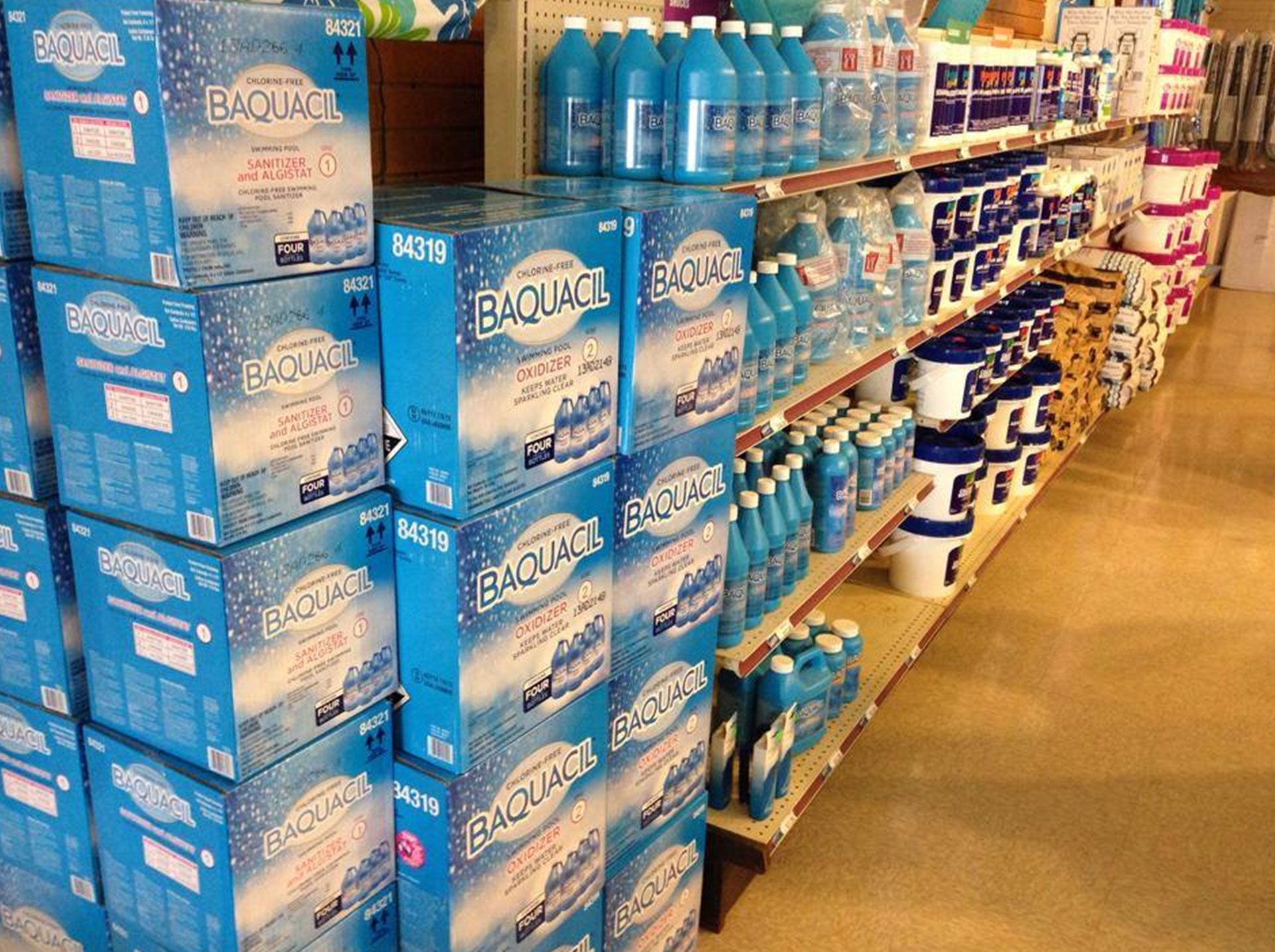 Shelves stocked with blue Baquacil pool chemical products in a retail store.