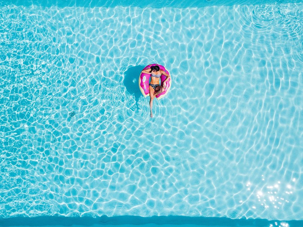 Woman floats on a pink inflatable ring in a clear, blue swimming pool.