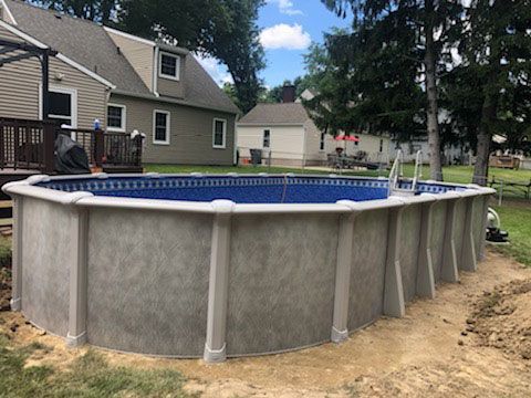 Above-ground pool in a backyard, with a house and trees in the background. The pool has a ladder.