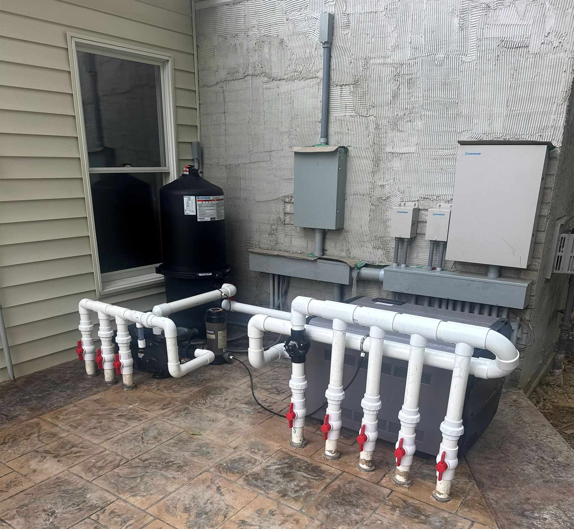 Pool equipment setup against a wall: pipes with valves, a pump, and a filter tank.