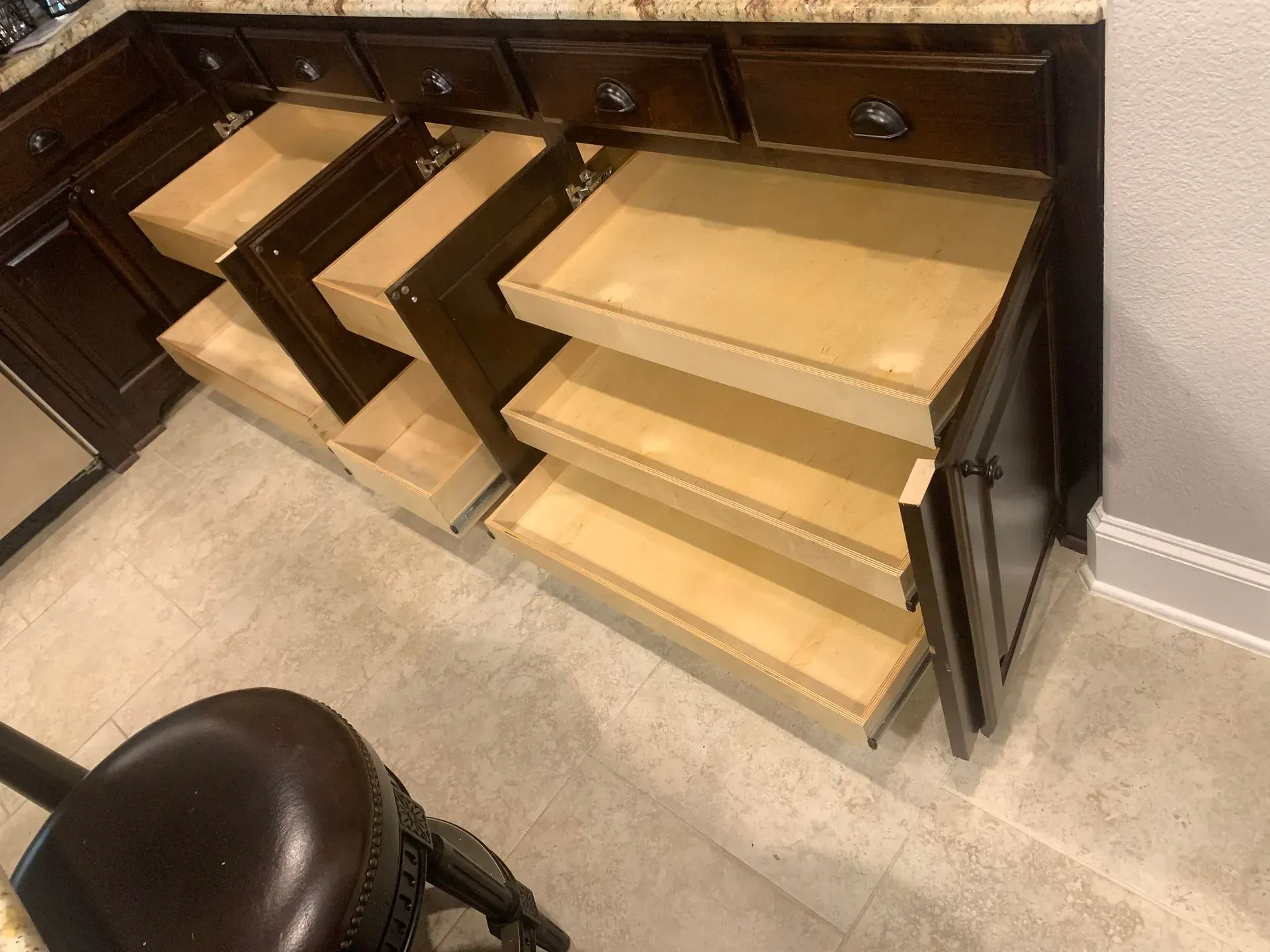 Kitchen cabinets with multiple open drawers, wooden interior, near a tile floor.