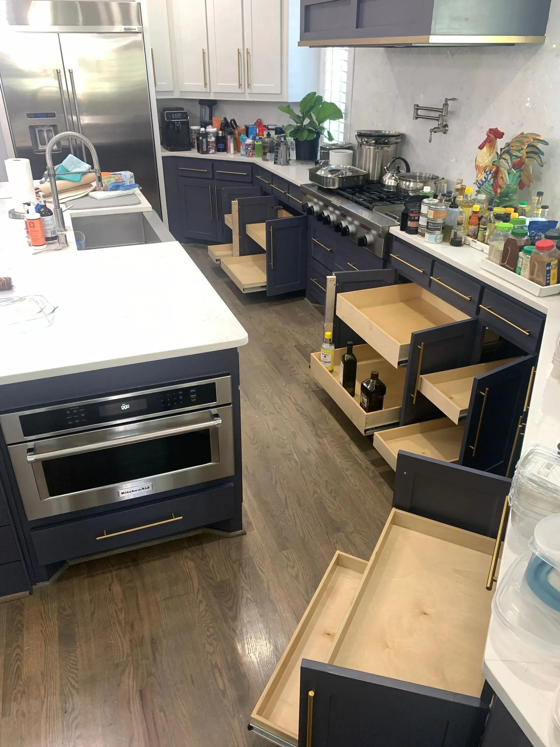 Navy blue kitchen with open pull-out cabinets, drawers, white countertops, and a stainless steel oven.