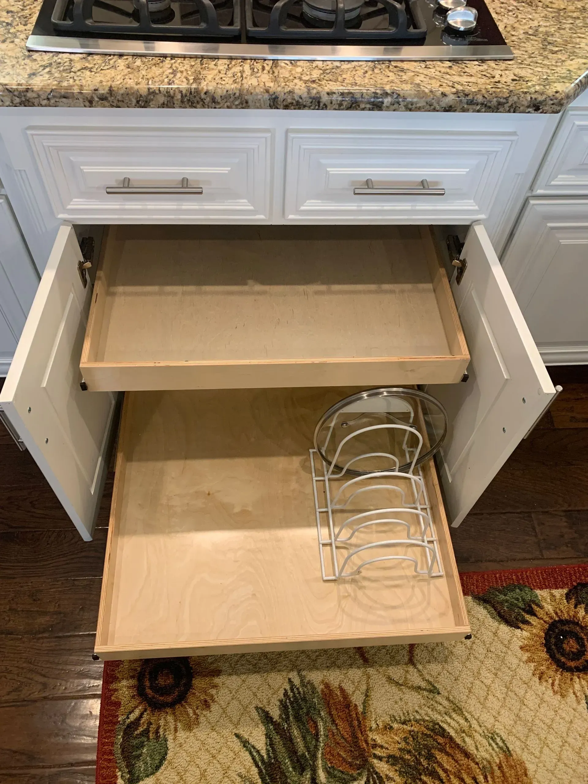 White kitchen cabinet with pull-out drawers; one open with a pot lid organizer, wood and white.