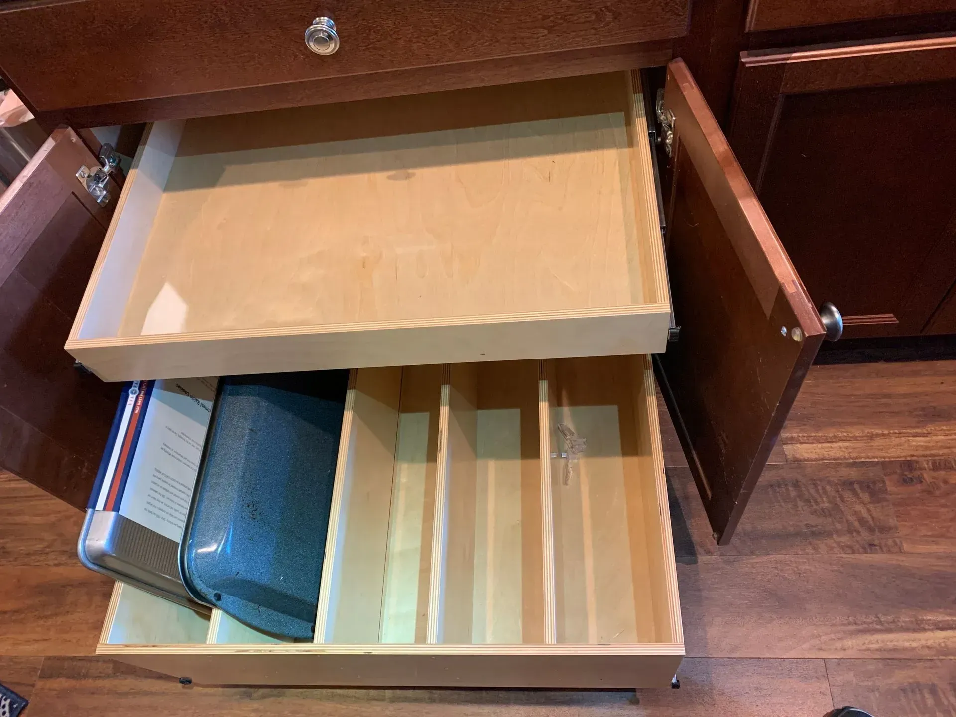 Open kitchen cabinet with two wooden drawers; one holds utensils.