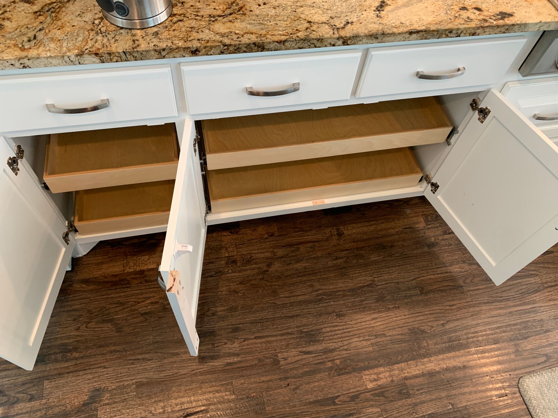 White kitchen cabinets with open doors, pull-out shelves, and granite countertop.