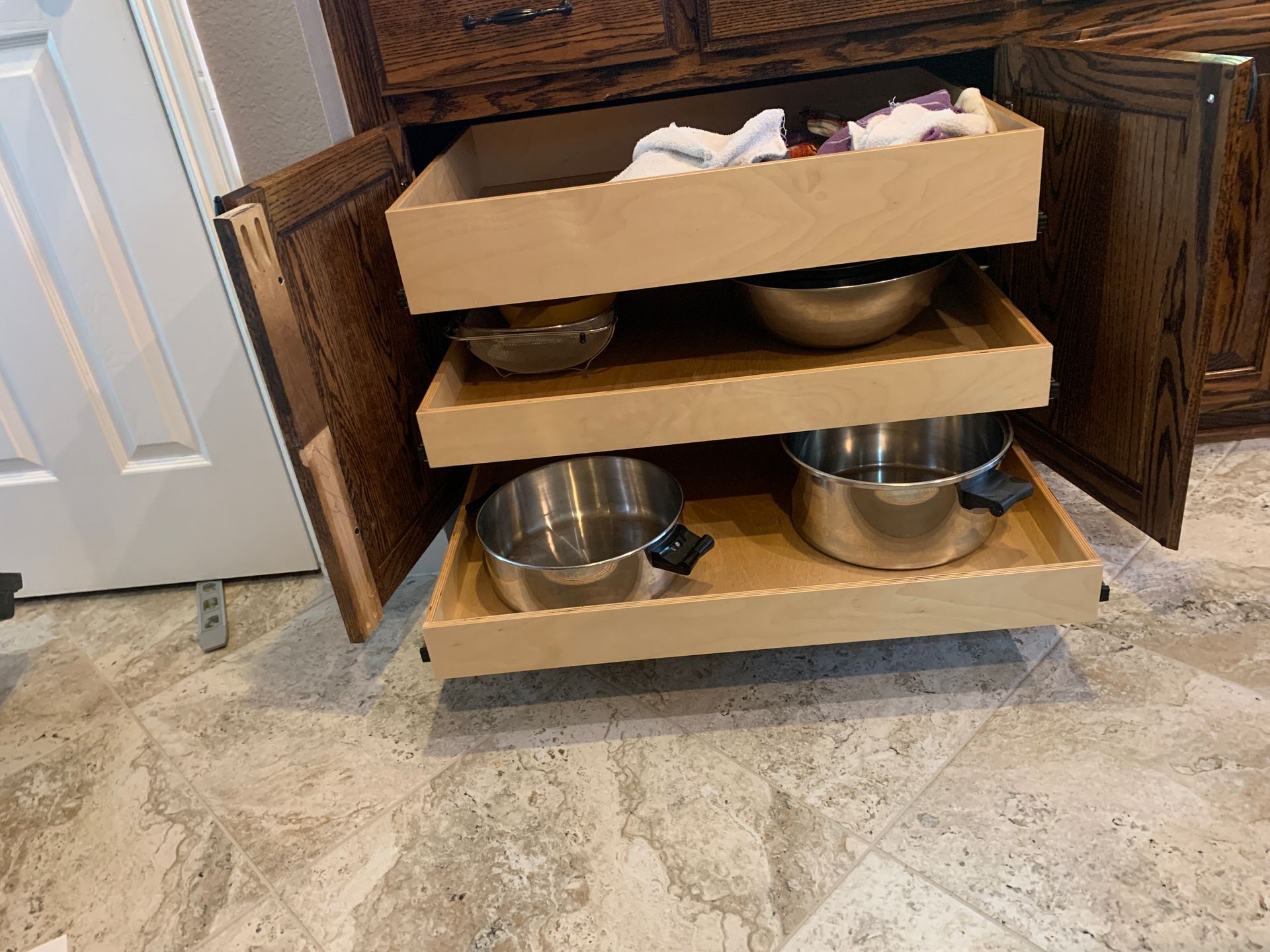 Pull-out drawers in a kitchen cabinet, containing mixing bowls and cookware.