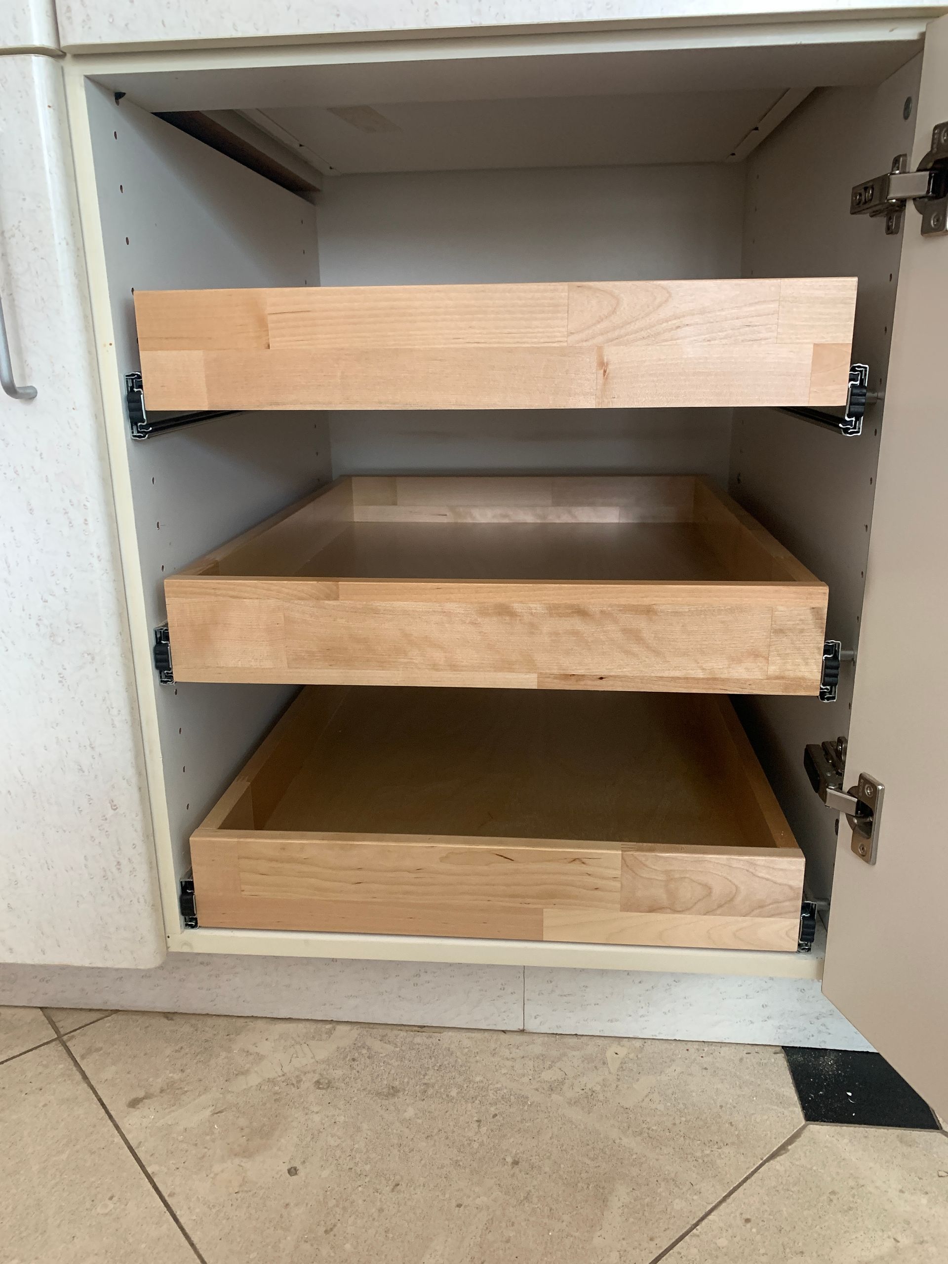 Three wooden pull-out shelves inside a white cabinet.