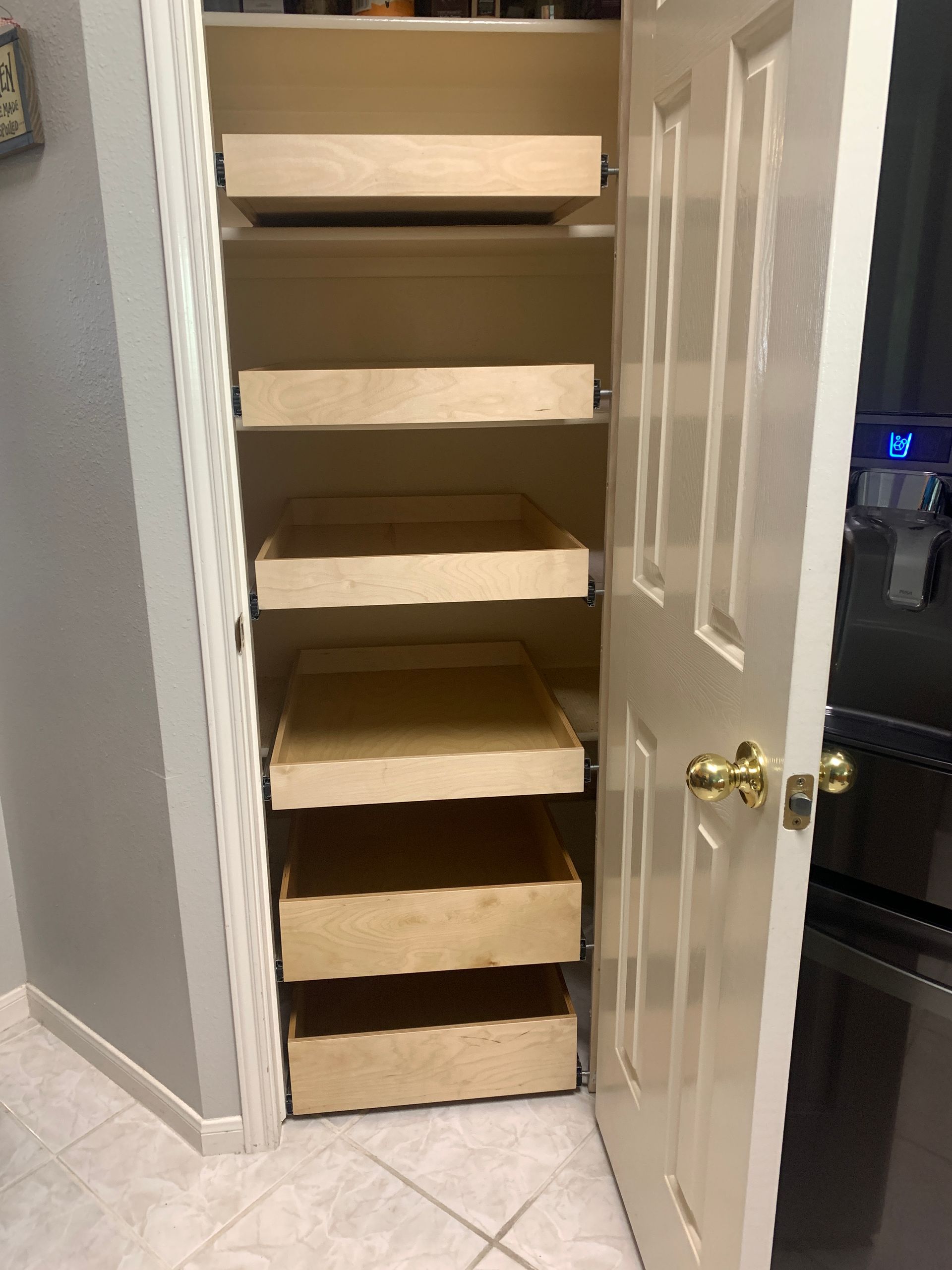Pantry with pull-out shelves; light wood construction in a white-walled closet.