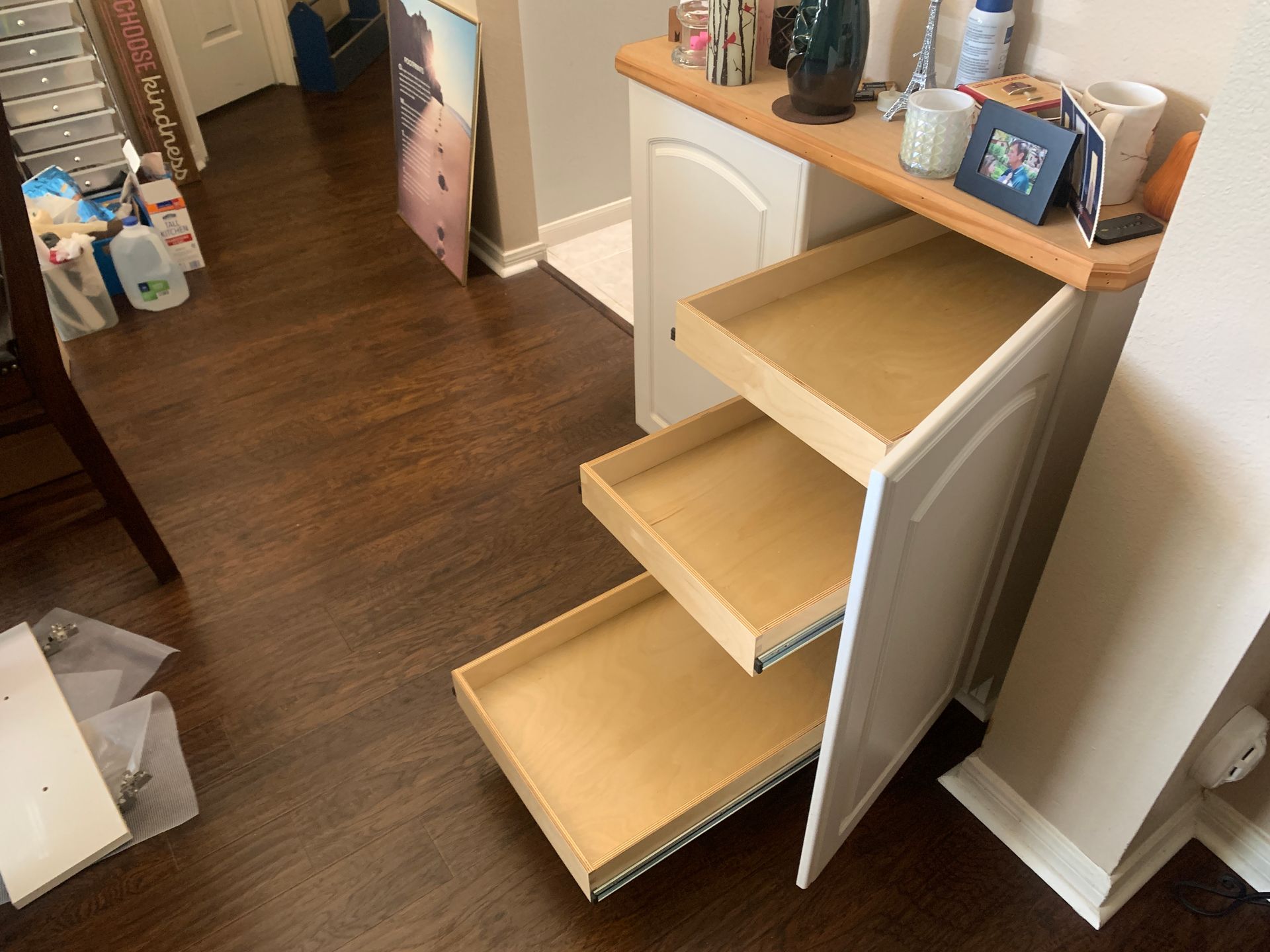 White cabinet with three open drawers on a wooden floor. Various items rest on the cabinet top.