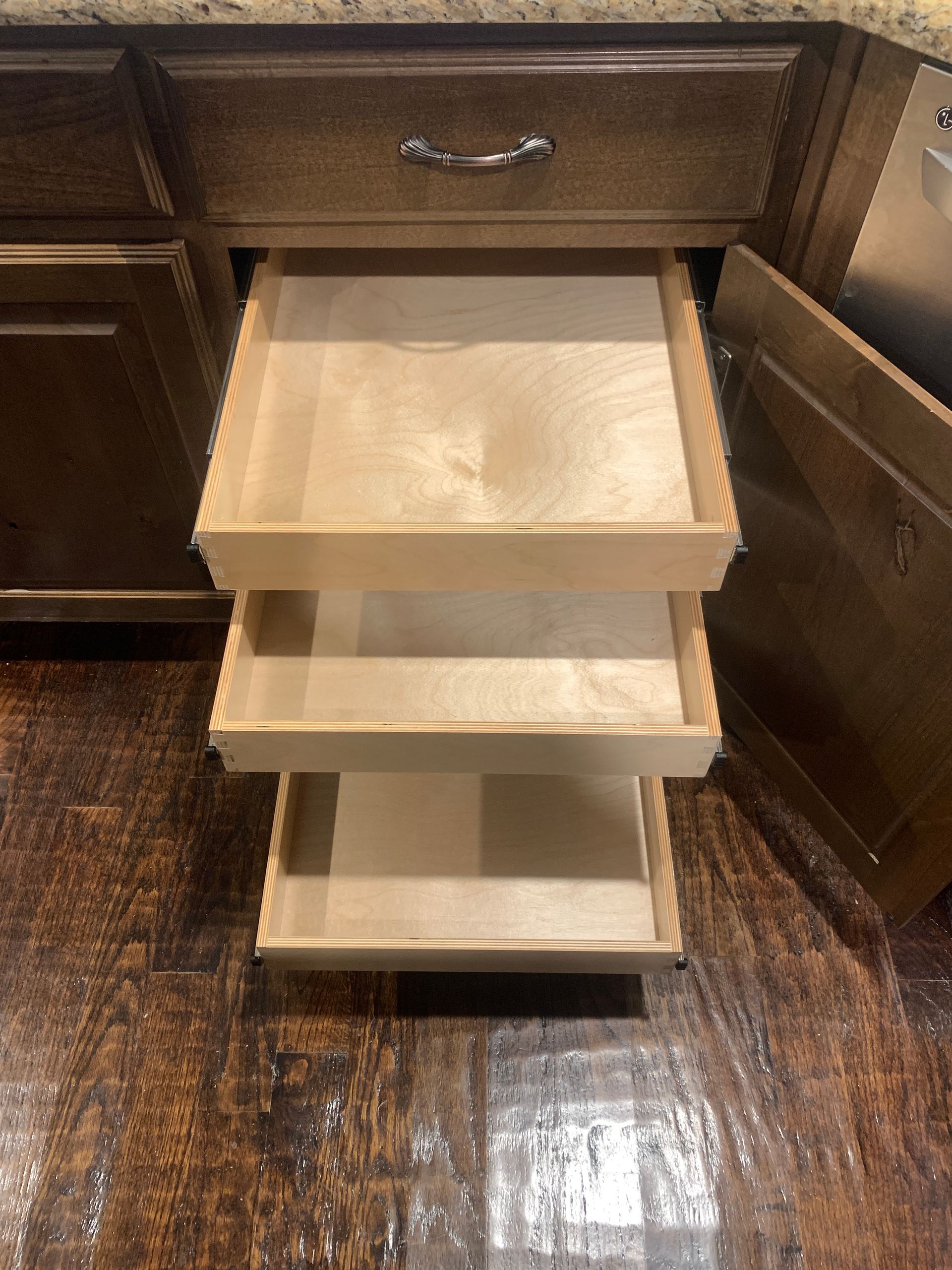 Open kitchen cabinet with three pull-out wooden drawers.