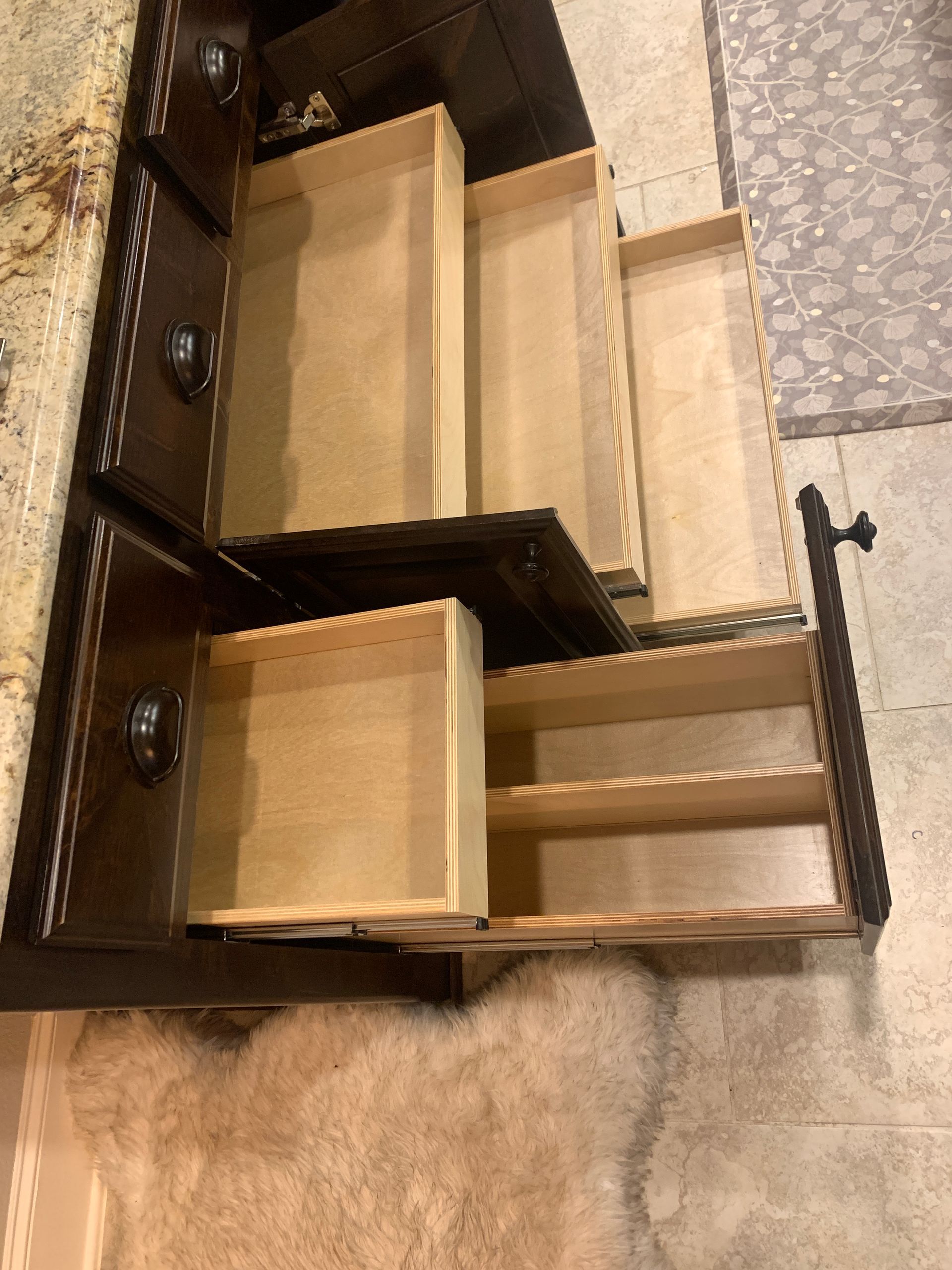 Open drawers in a dark brown dresser against a patterned floor and a granite countertop.