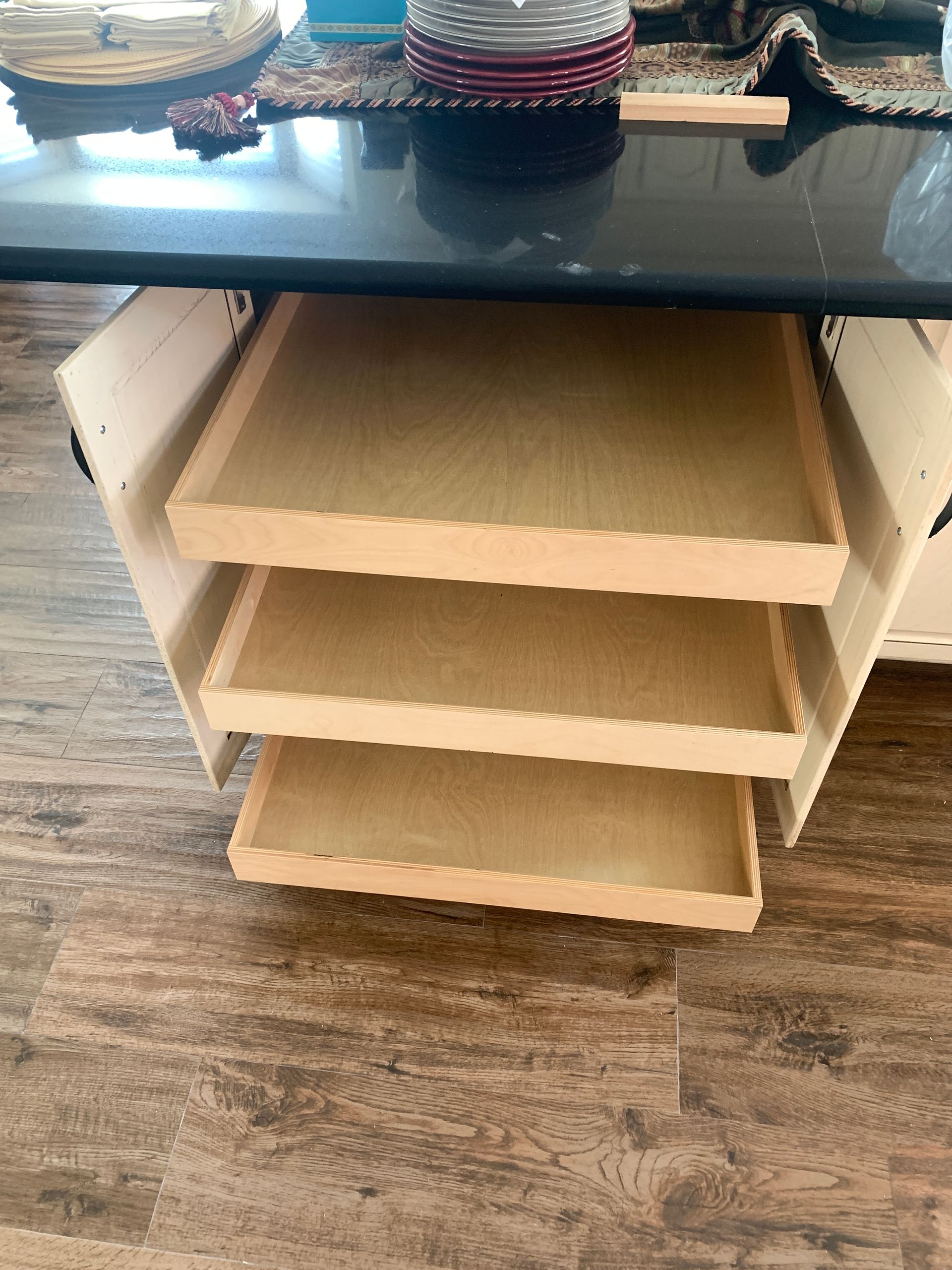 Three pull-out shelves inside a white kitchen cabinet, under a black countertop. Wooden shelves.