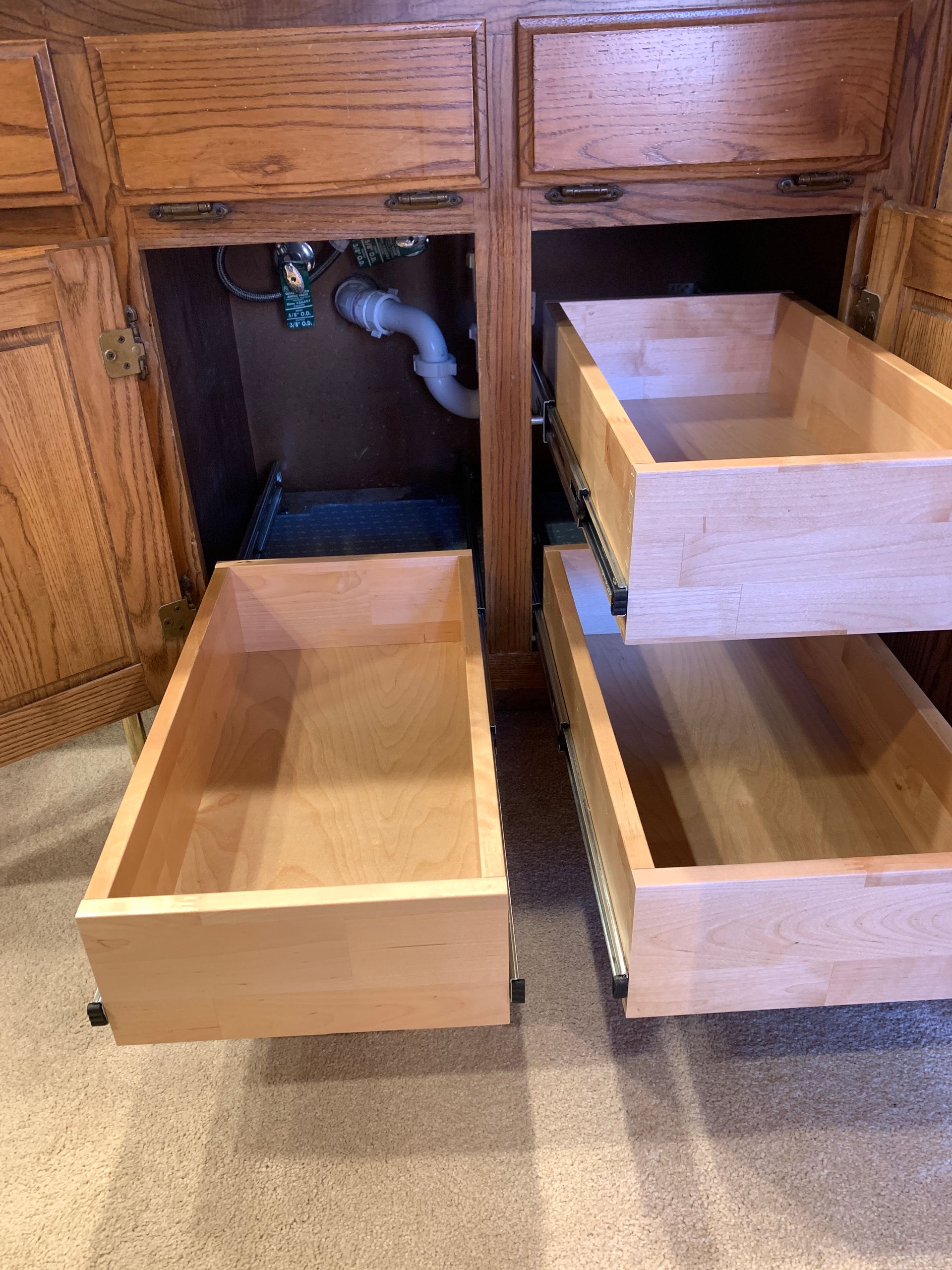 Wooden kitchen cabinet with open drawers, plumbing visible.