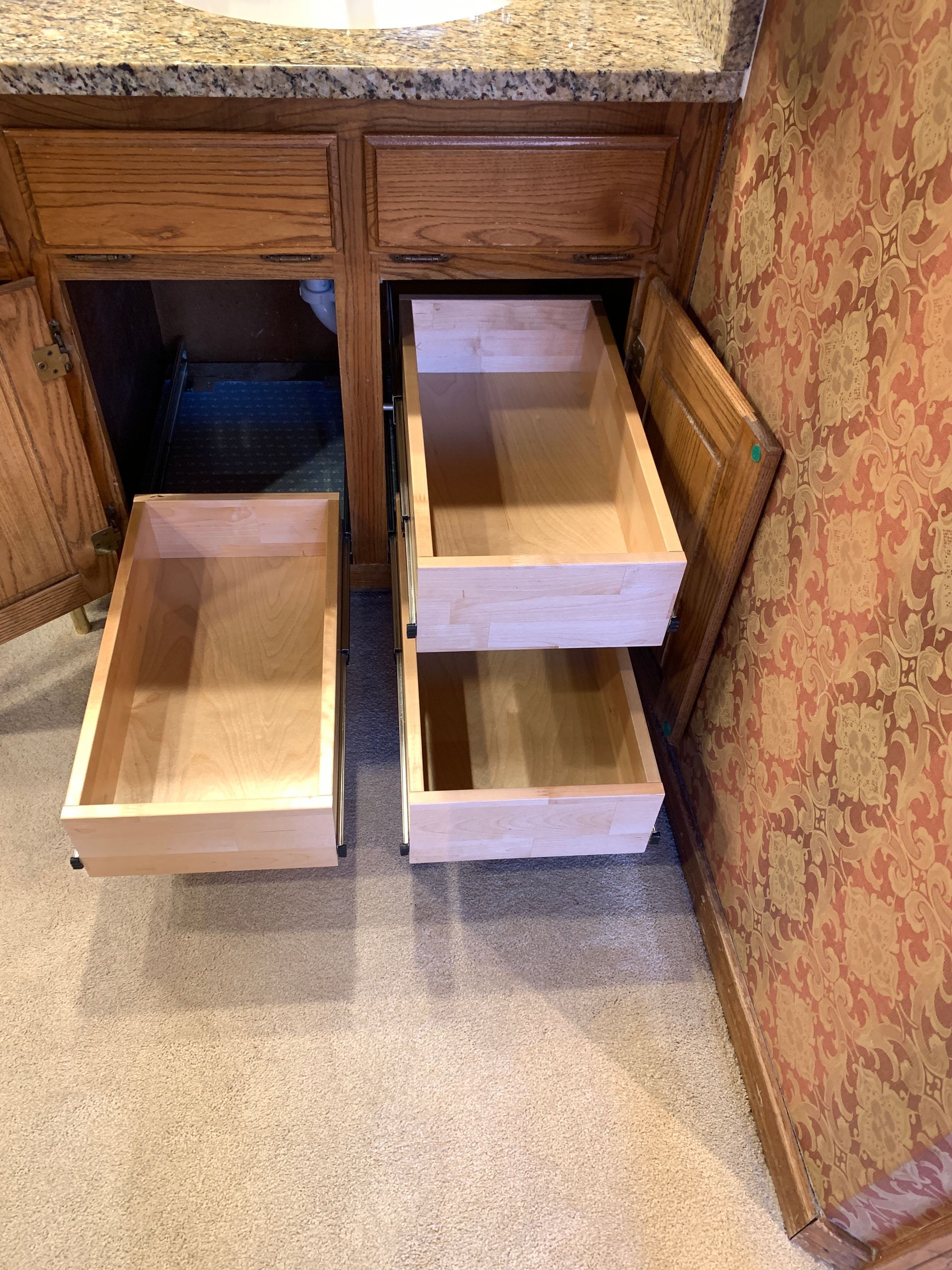 Wooden bathroom vanity with open drawers and a cabinet, on a tan carpet floor.