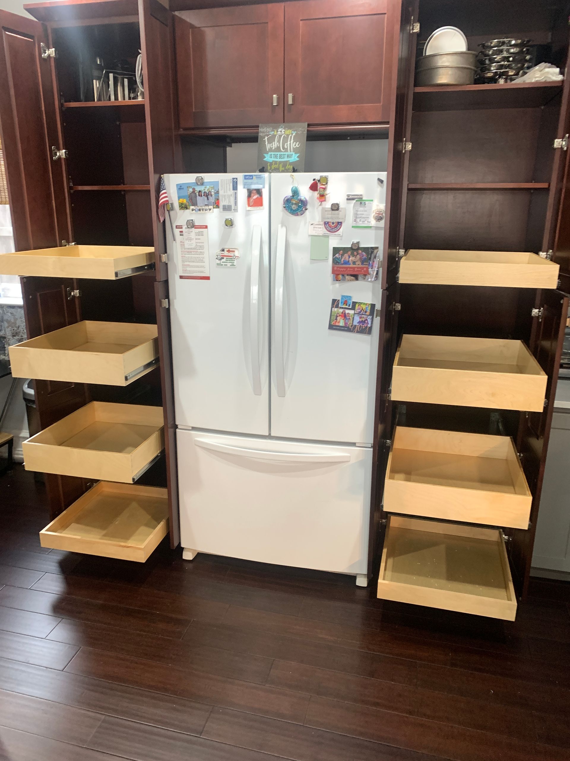 Wooden kitchen cabinets with pull-out shelves flanking a white refrigerator. Dark wood floors.