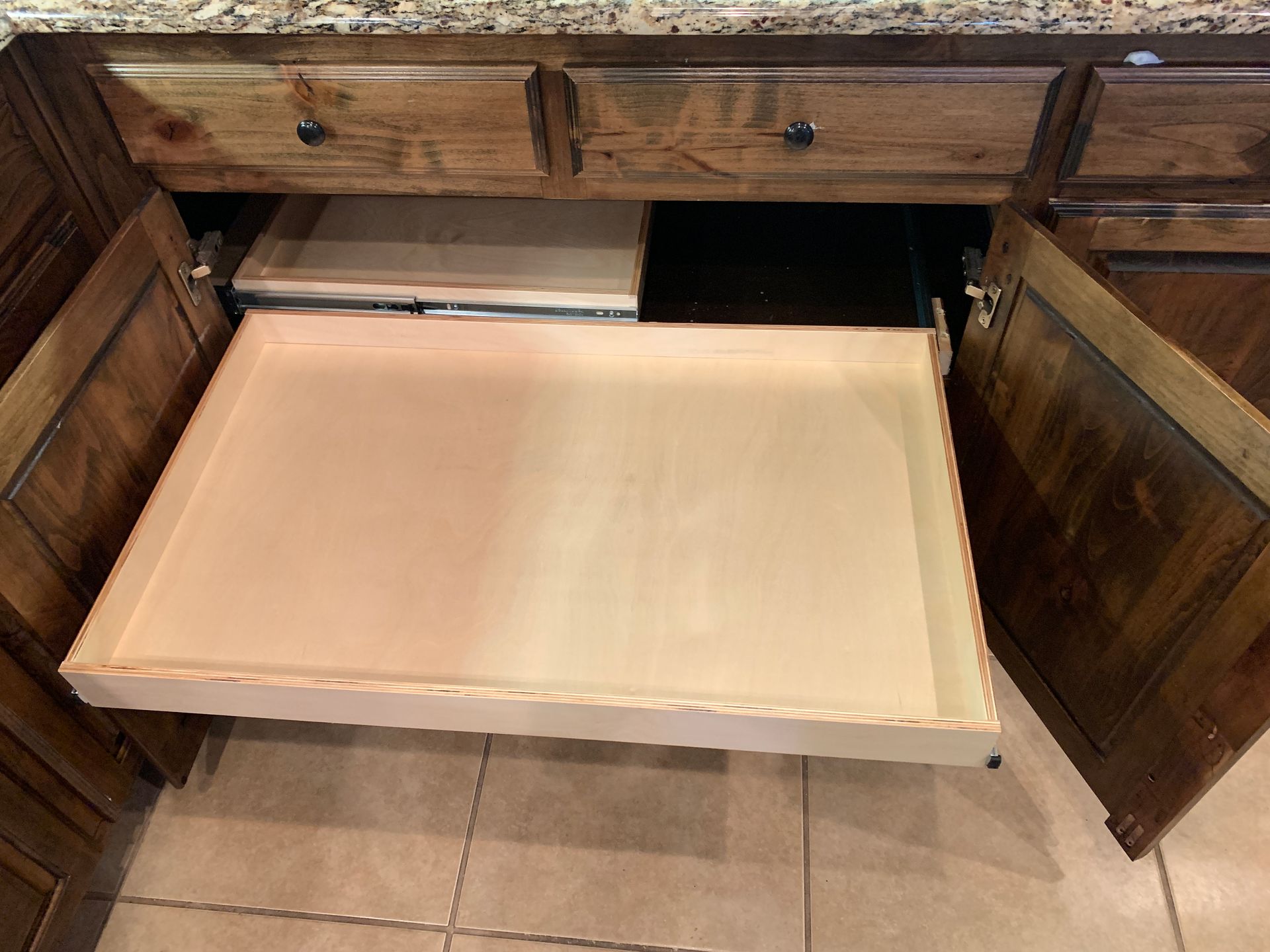 A wooden cabinet with a pull-out drawer extended; light wooden drawer on the bottom and a smaller one above it.