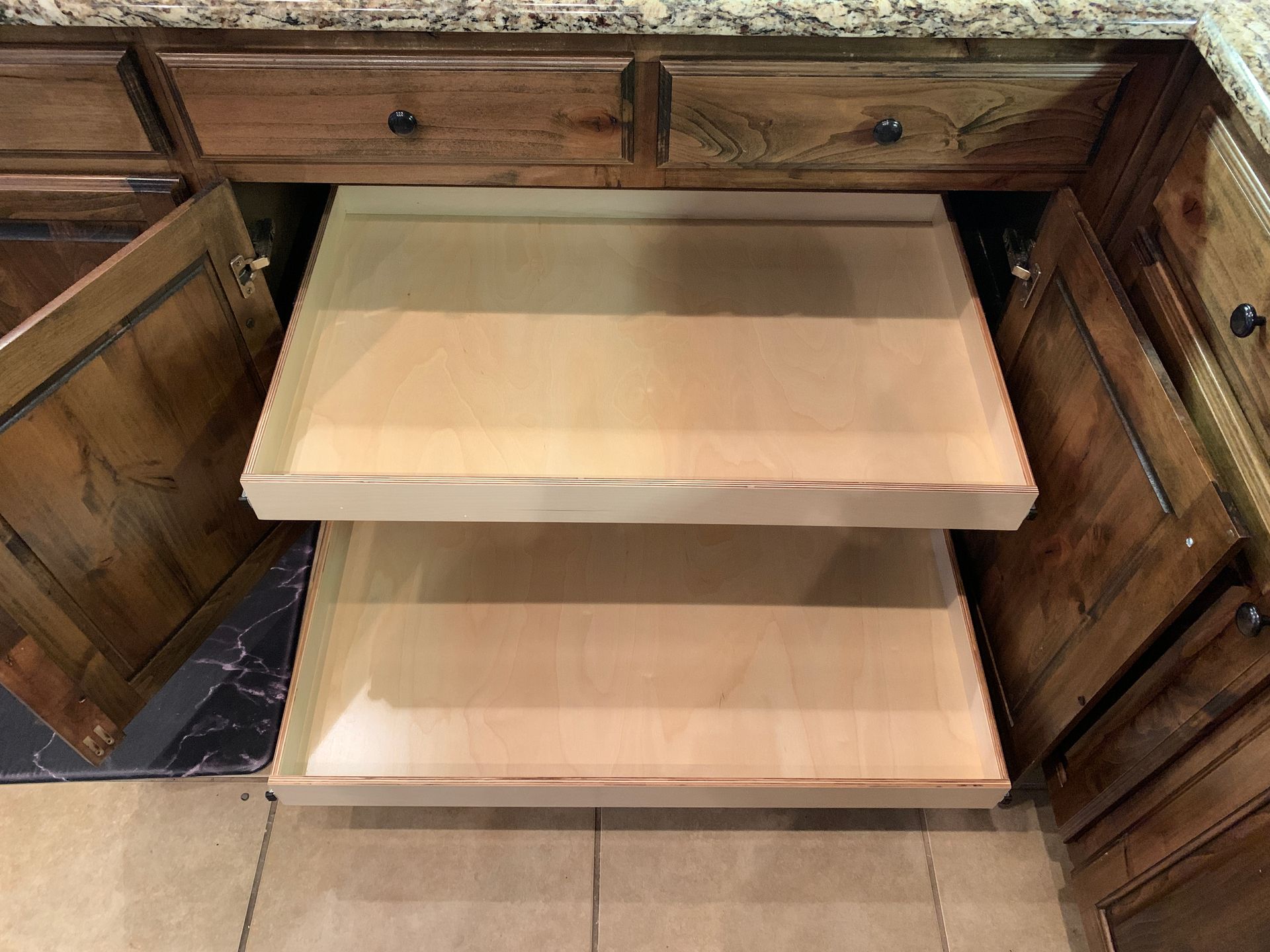 Two pull-out wooden shelves inside a kitchen cabinet, visible with doors open.