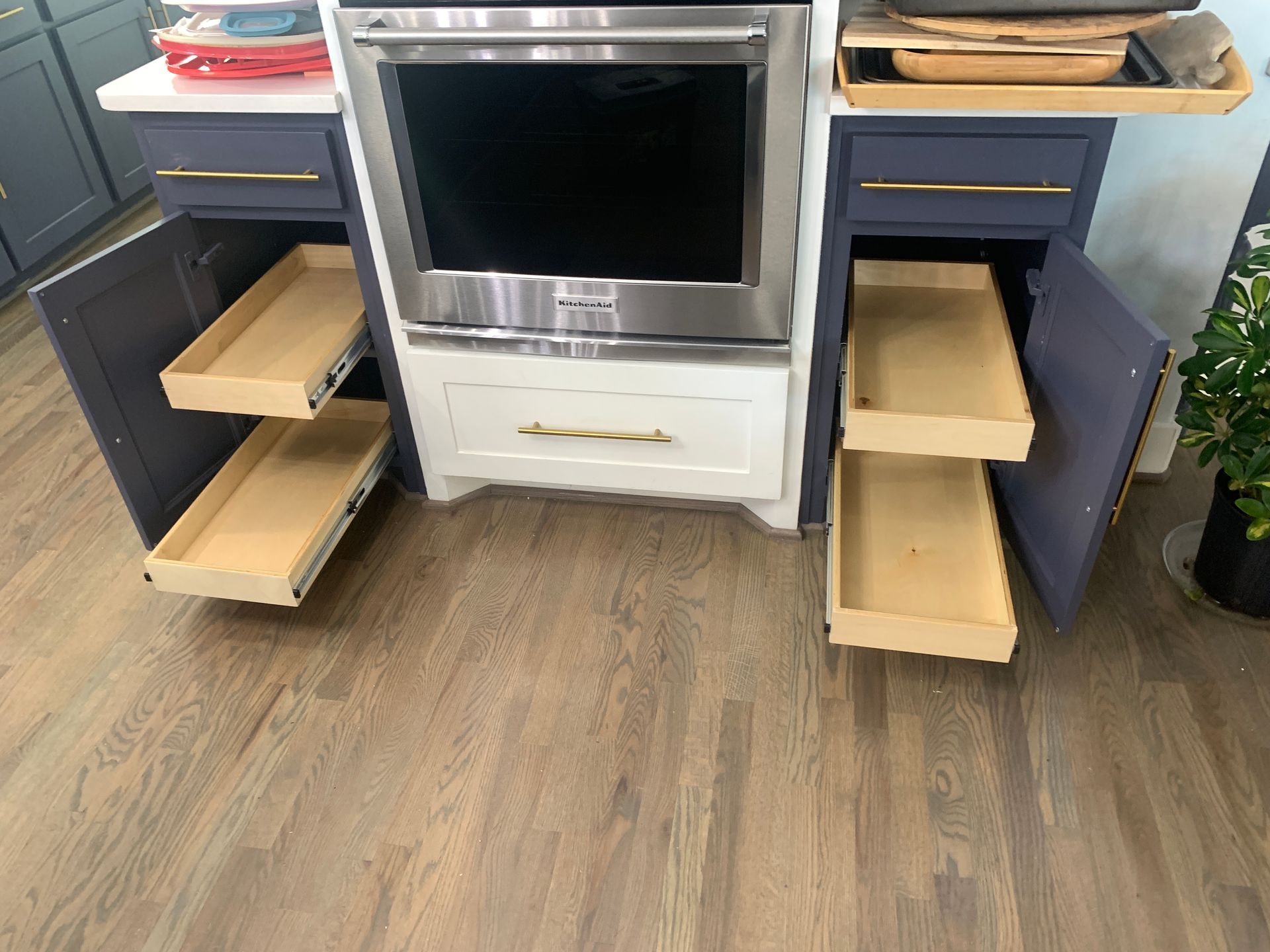 Kitchen cabinetry with oven. Blue cabinets with pull-out drawers flank the oven. Wooden floor.
