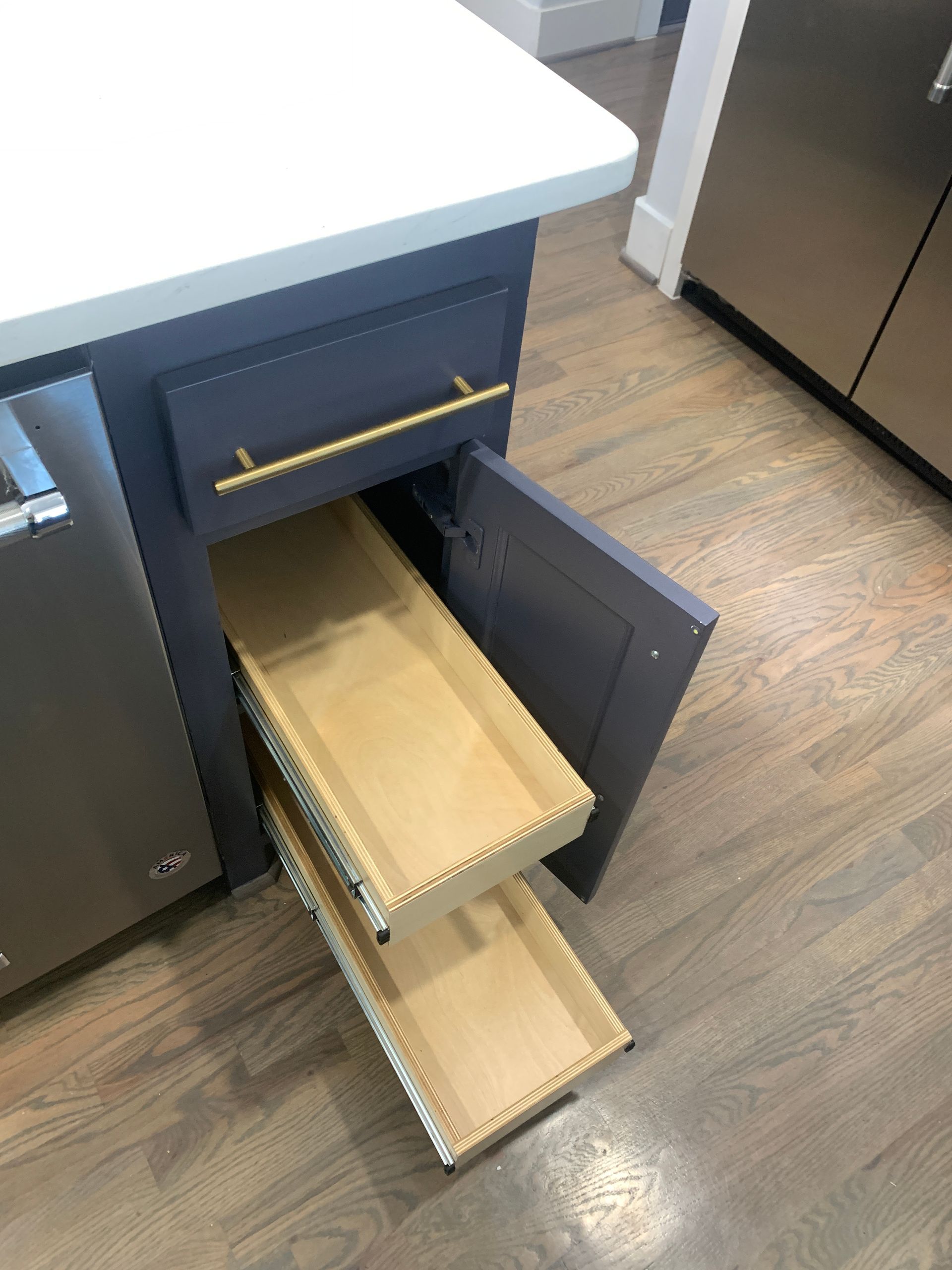 Navy kitchen cabinet with gold hardware and pull-out drawers, partially open.