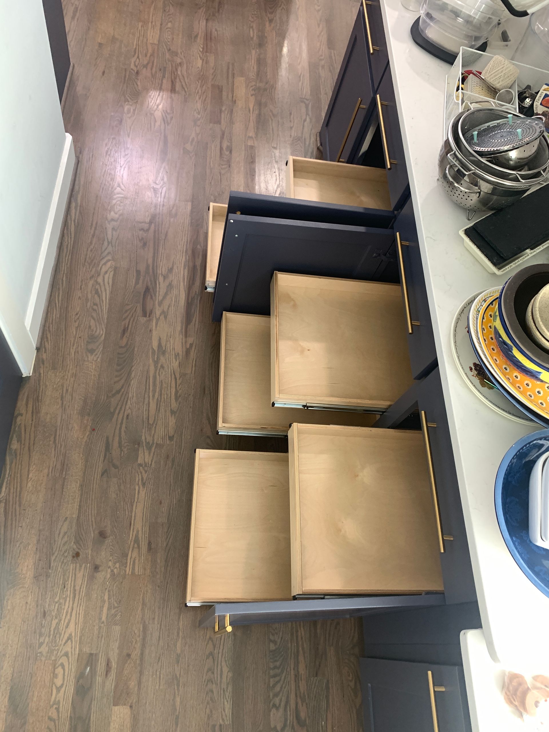 Open kitchen drawers, navy cabinets, wooden floors.