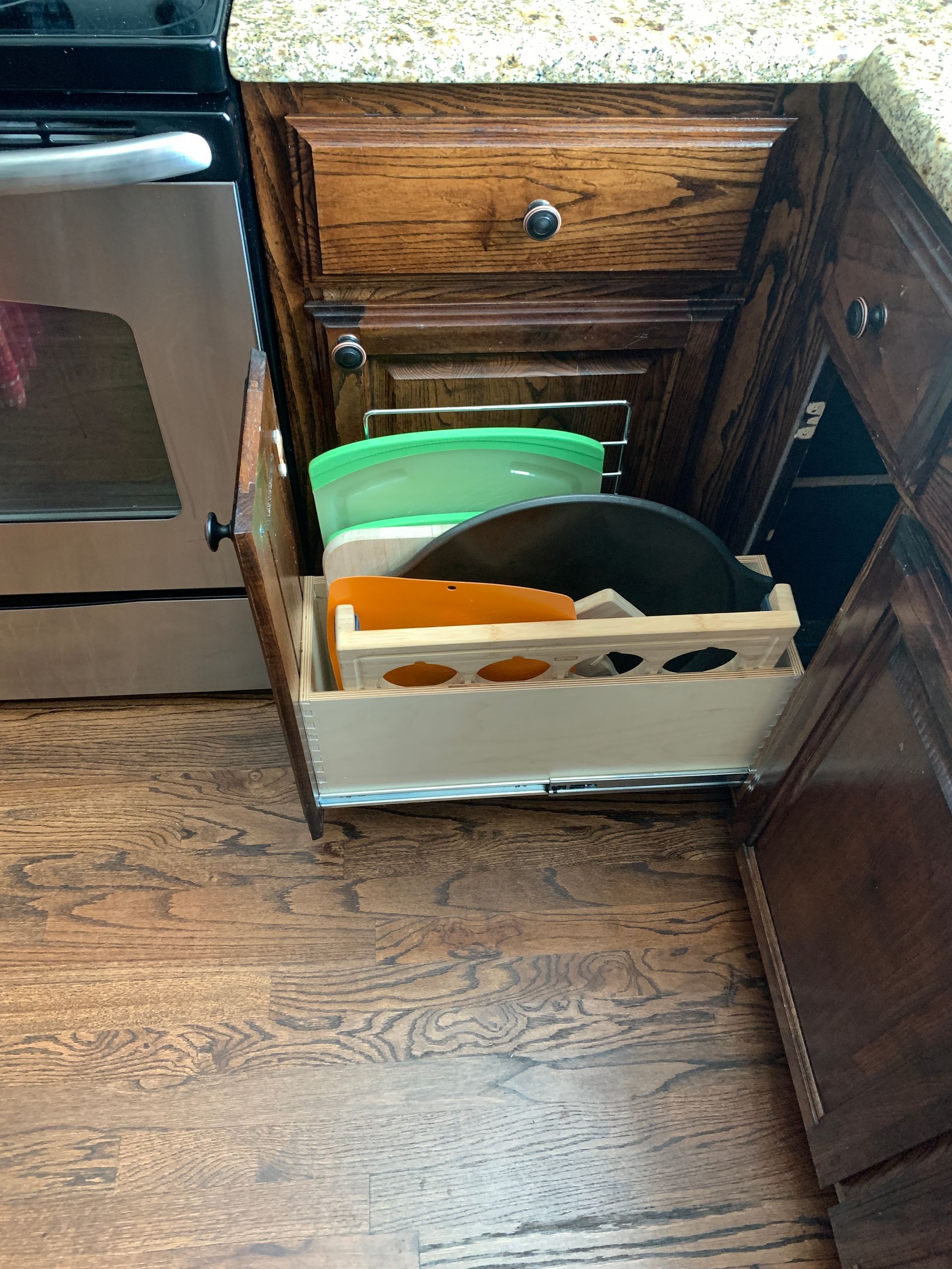 Open kitchen drawer with pans, lids, and cutting boards; located next to the stove.
