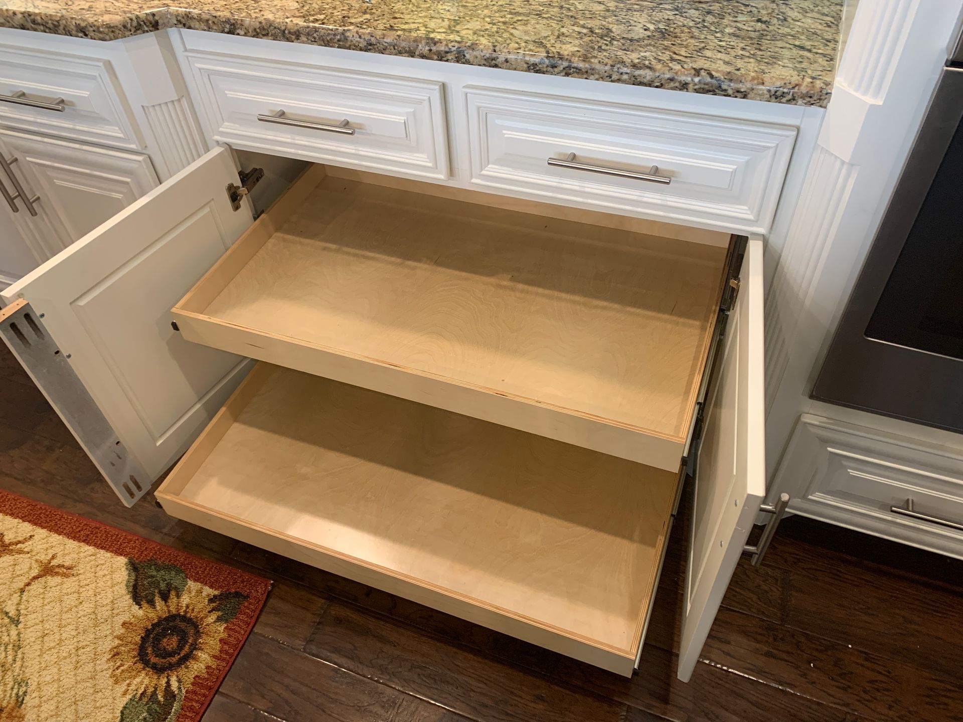 White kitchen cabinet with two pull-out shelves. Doors open, revealing the wooden shelves.