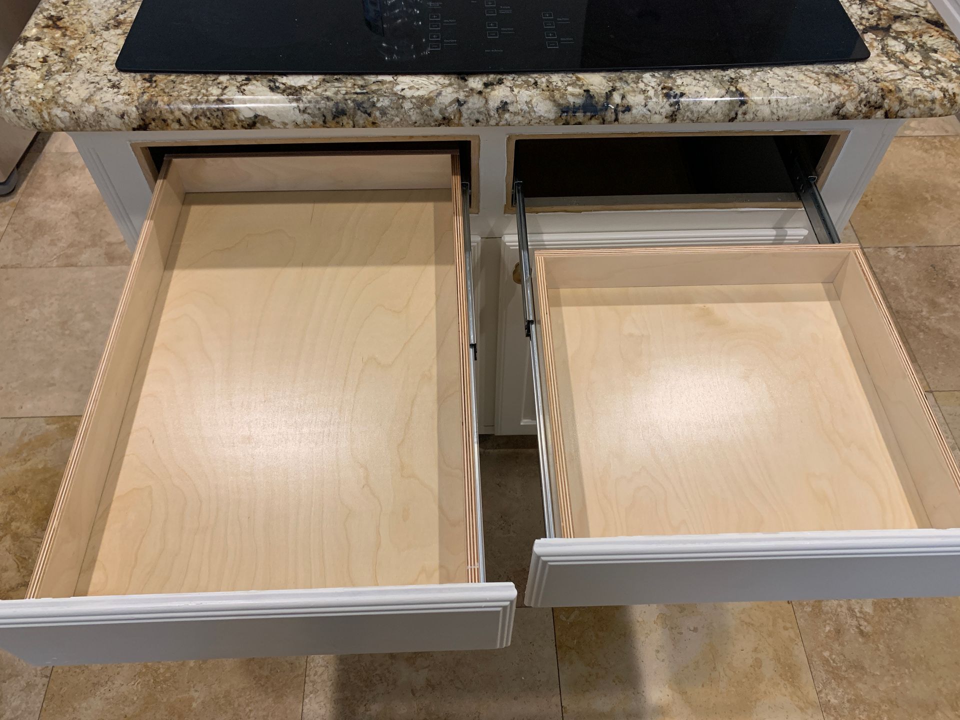 Two open white kitchen drawers, light wood interiors, under a countertop.