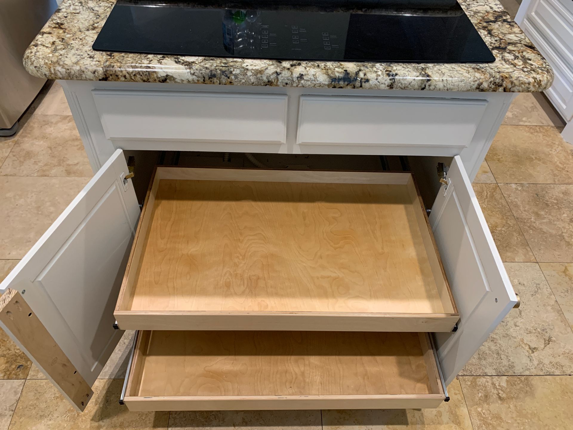 White kitchen island with open cabinet doors, revealing two pull-out trays, under a stovetop.