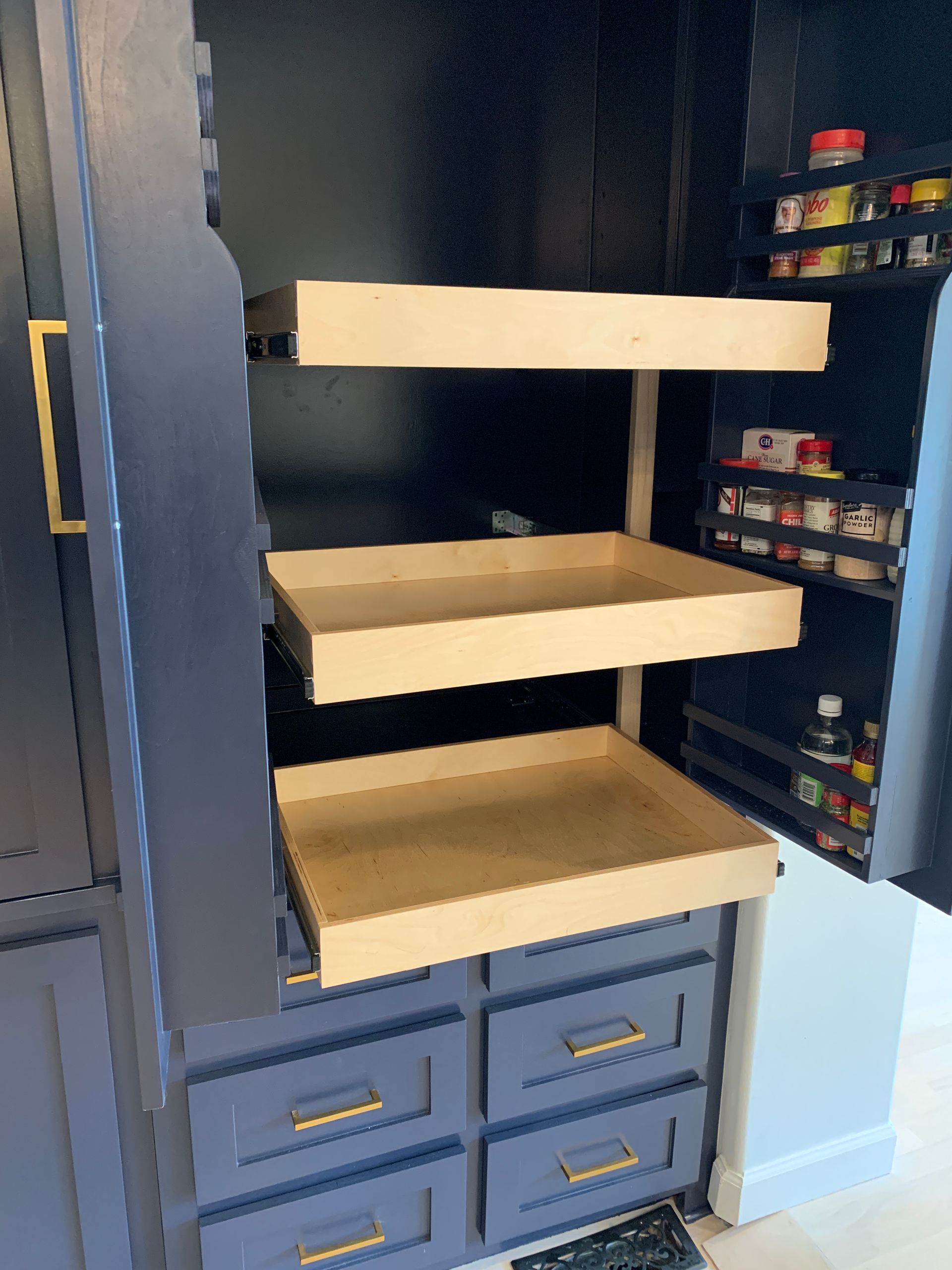 Blue pantry with pull-out shelves and drawers. Contains spices on the door, with gold handles.