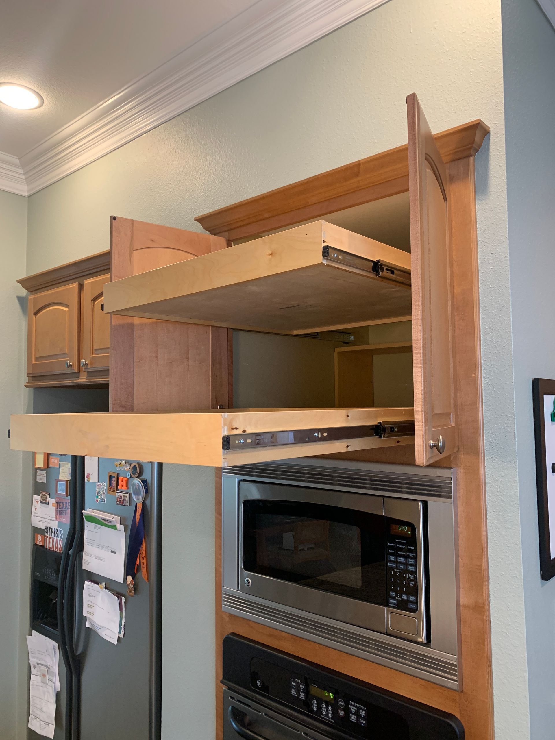 Open cabinet with pull-out shelves above a microwave and oven unit in a kitchen.