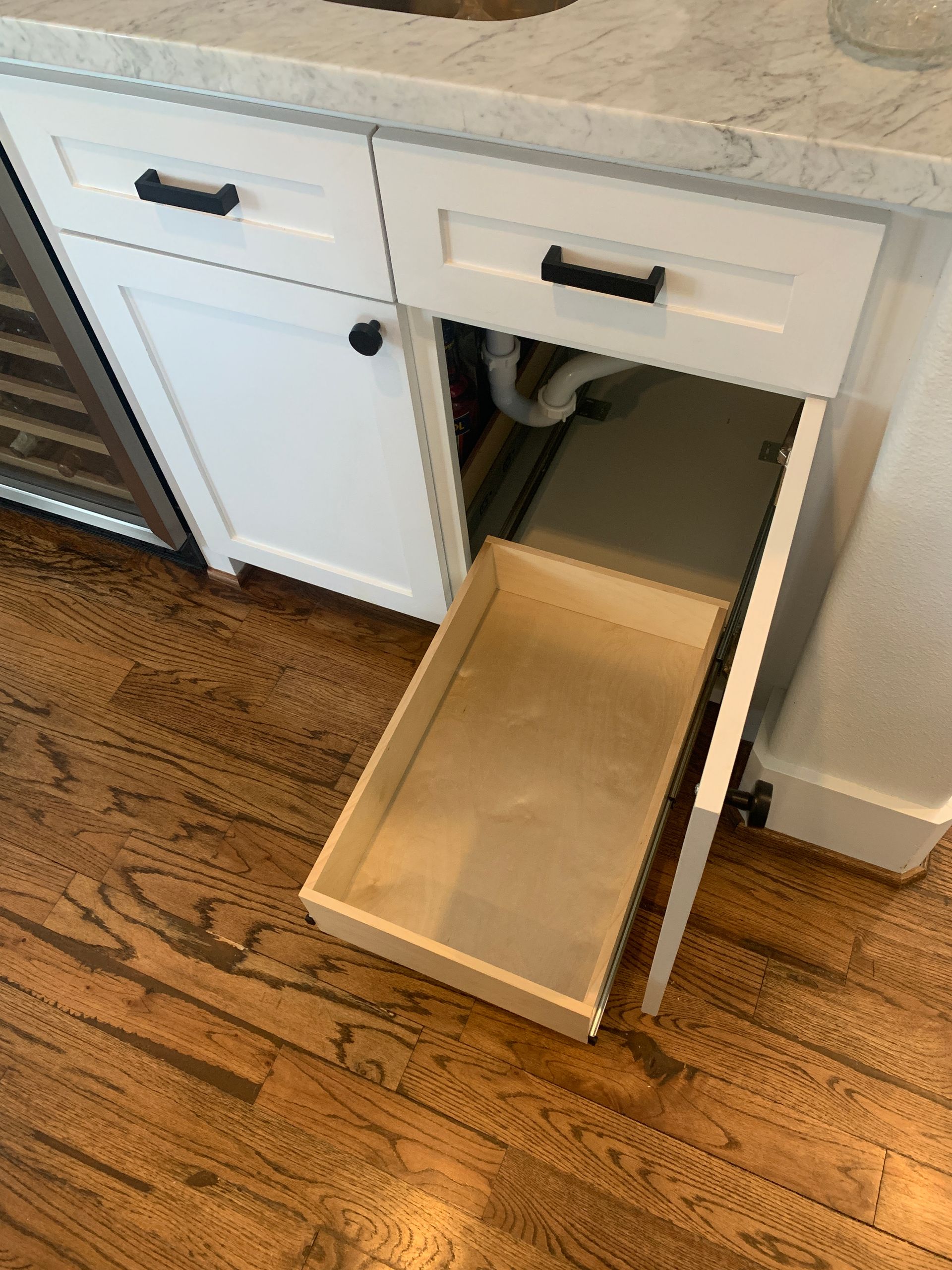 White cabinet with an open drawer, showing plumbing inside.