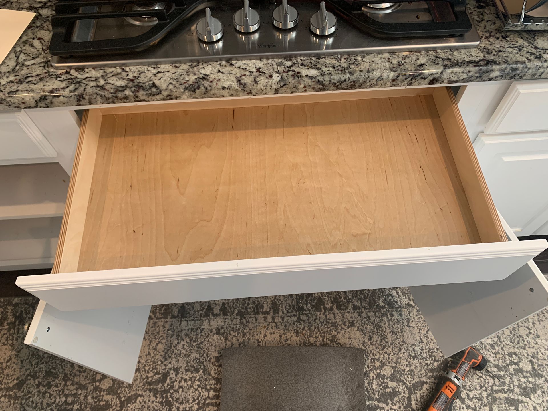 Open kitchen drawer, with a wooden interior and white trim, resting on a patterned rug.