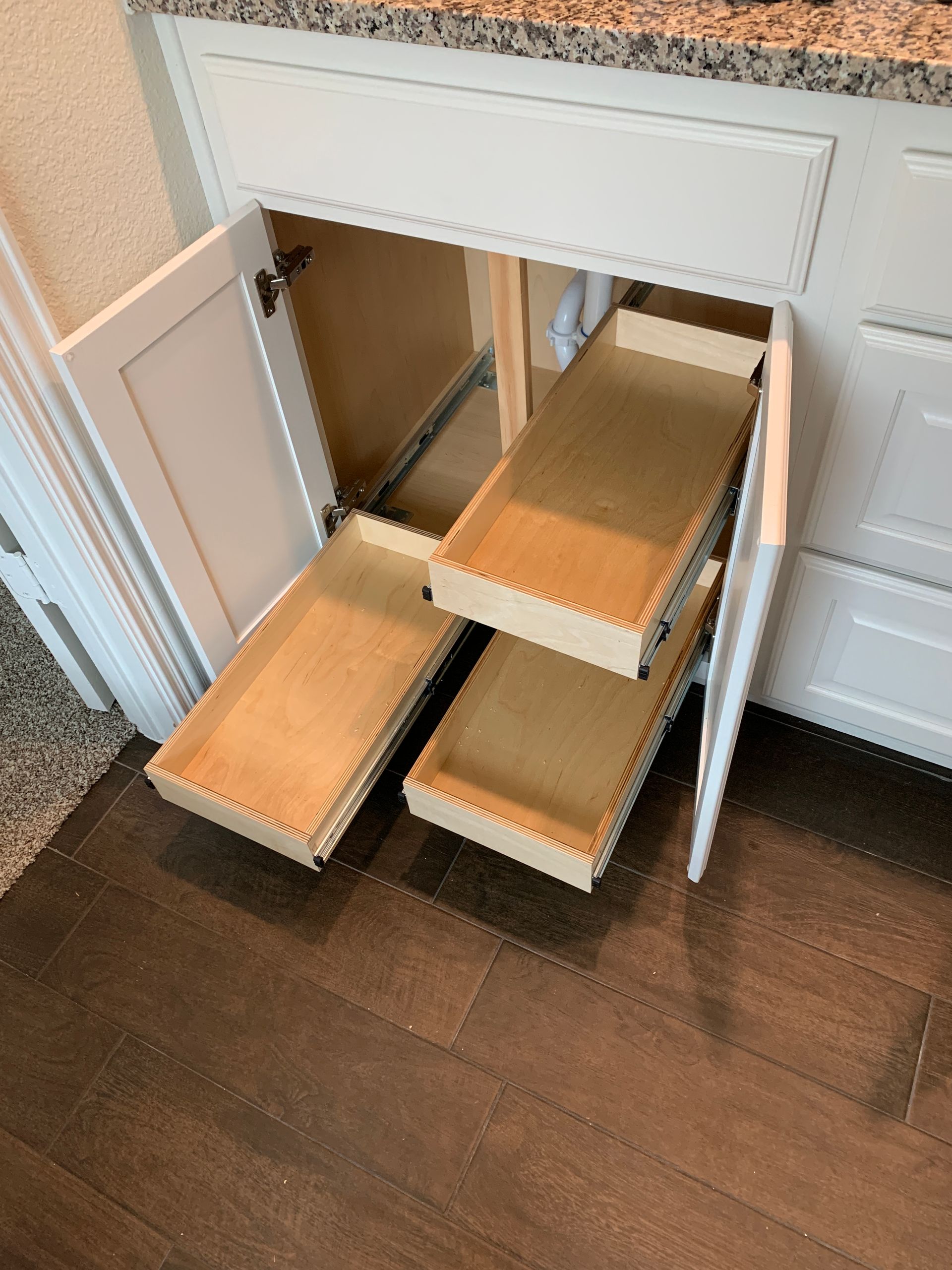 White cabinet with pull-out drawers, revealing plumbing.  Drawers are open on wooden floor.