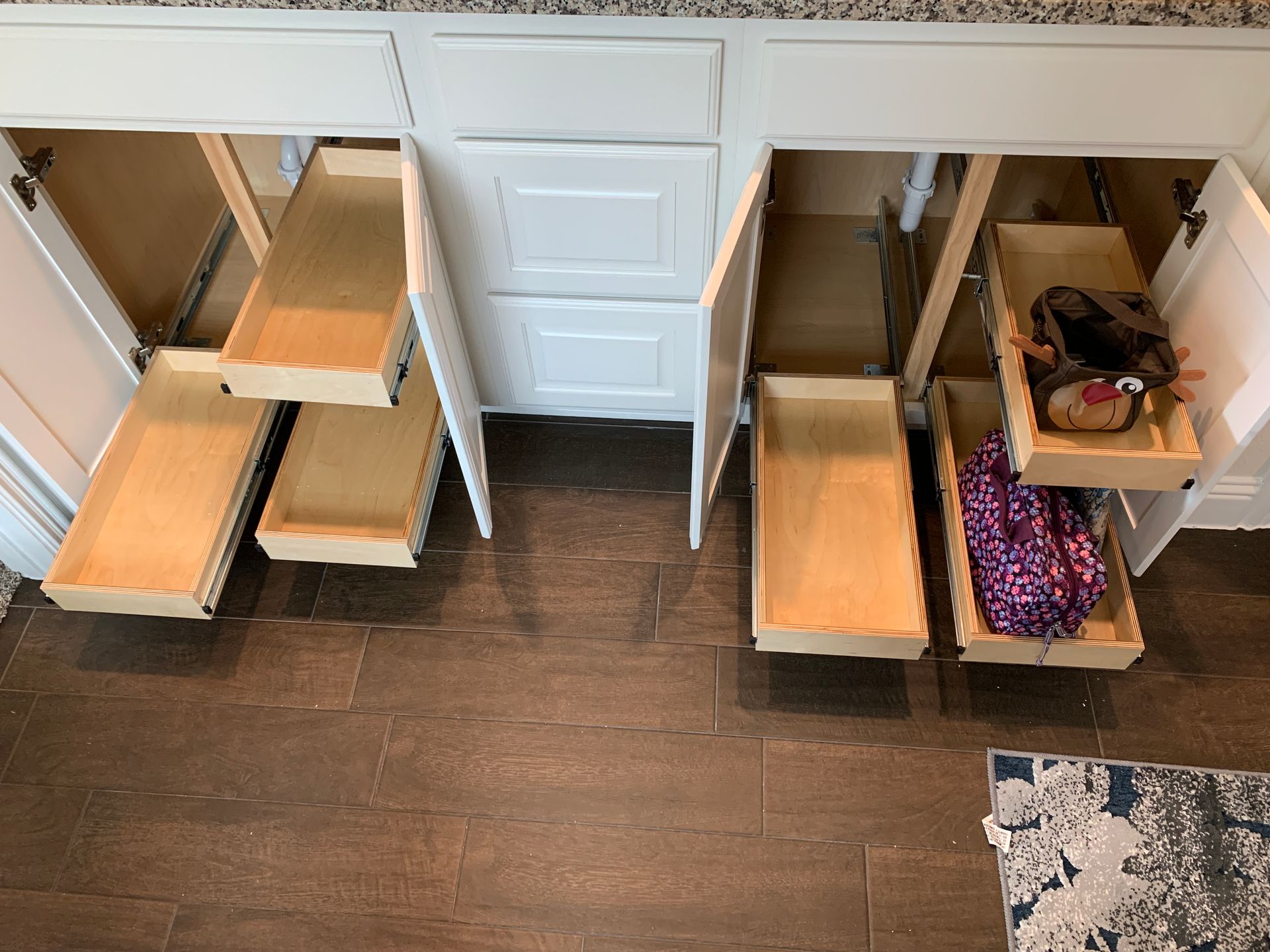 White bathroom vanity with pull-out drawers, open showing contents. Brown floor.