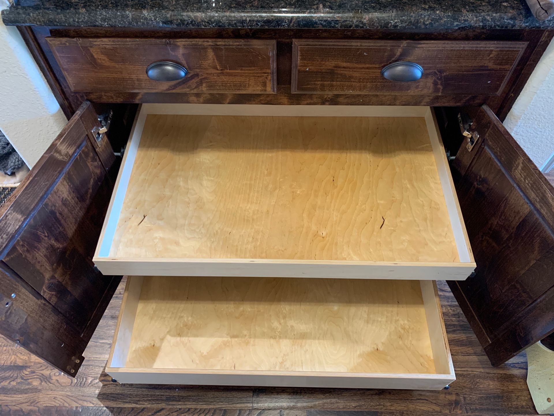 Open kitchen cabinet with two pull-out shelves; dark wood, light wood shelves.