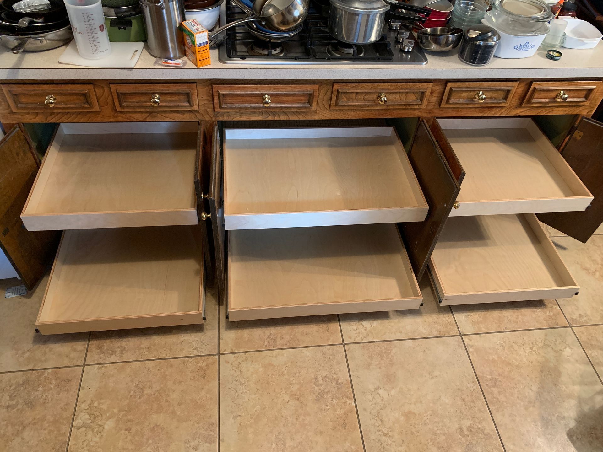 Kitchen cabinet with three pull-out shelves open, showing their interior surfaces. Brown floor.