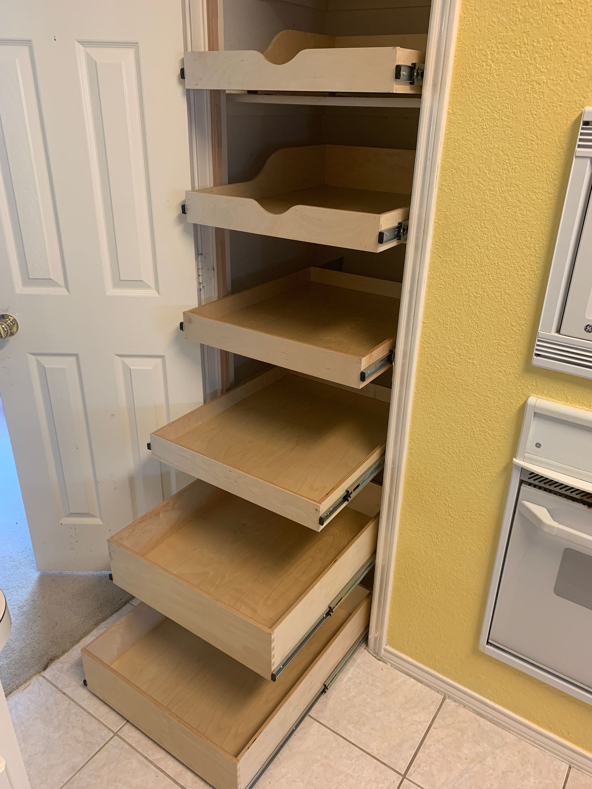 Wooden pull-out pantry shelves inside a kitchen closet next to a yellow wall.