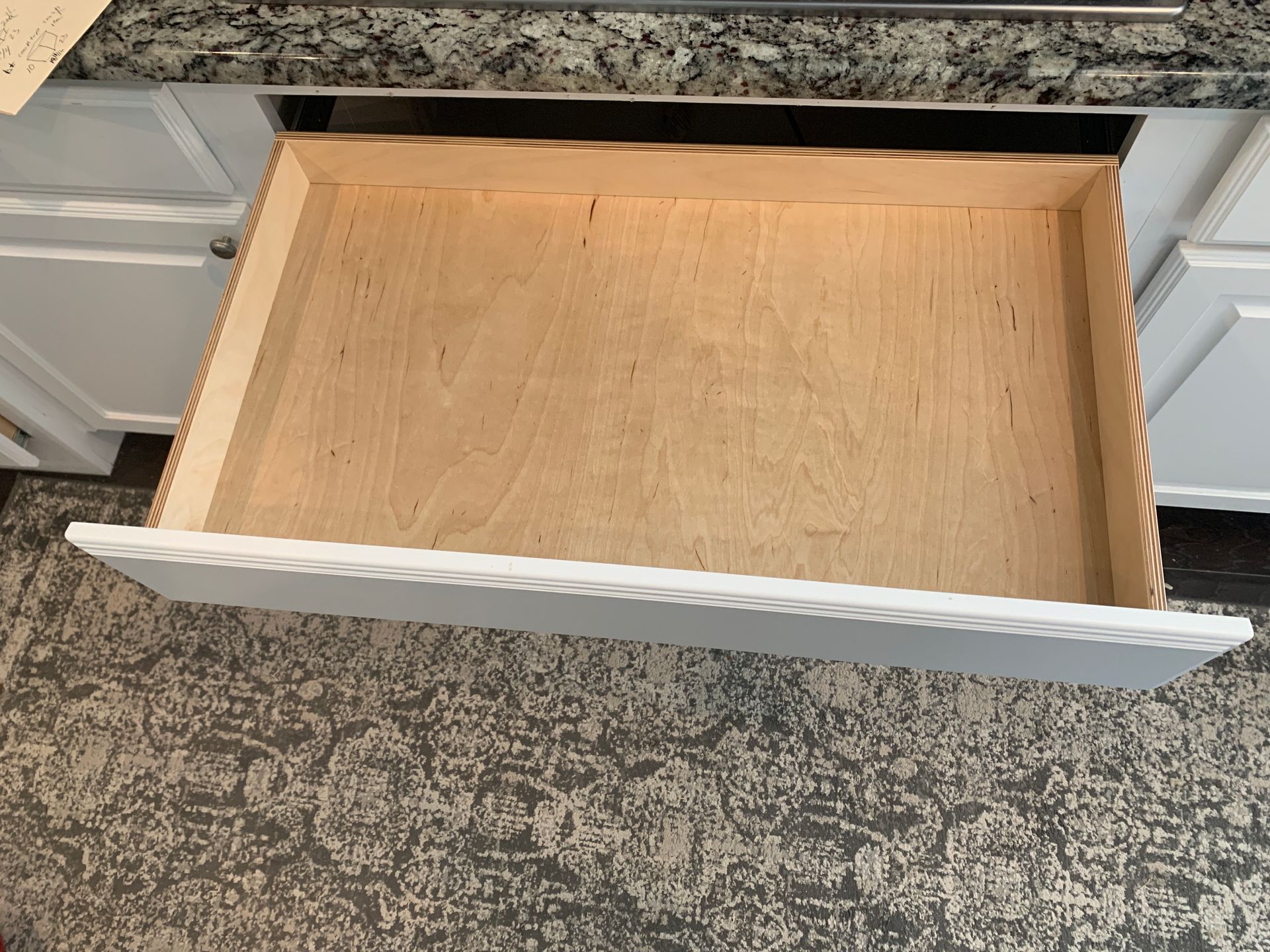 An empty kitchen drawer, pulled open. Light wood interior, white painted front.