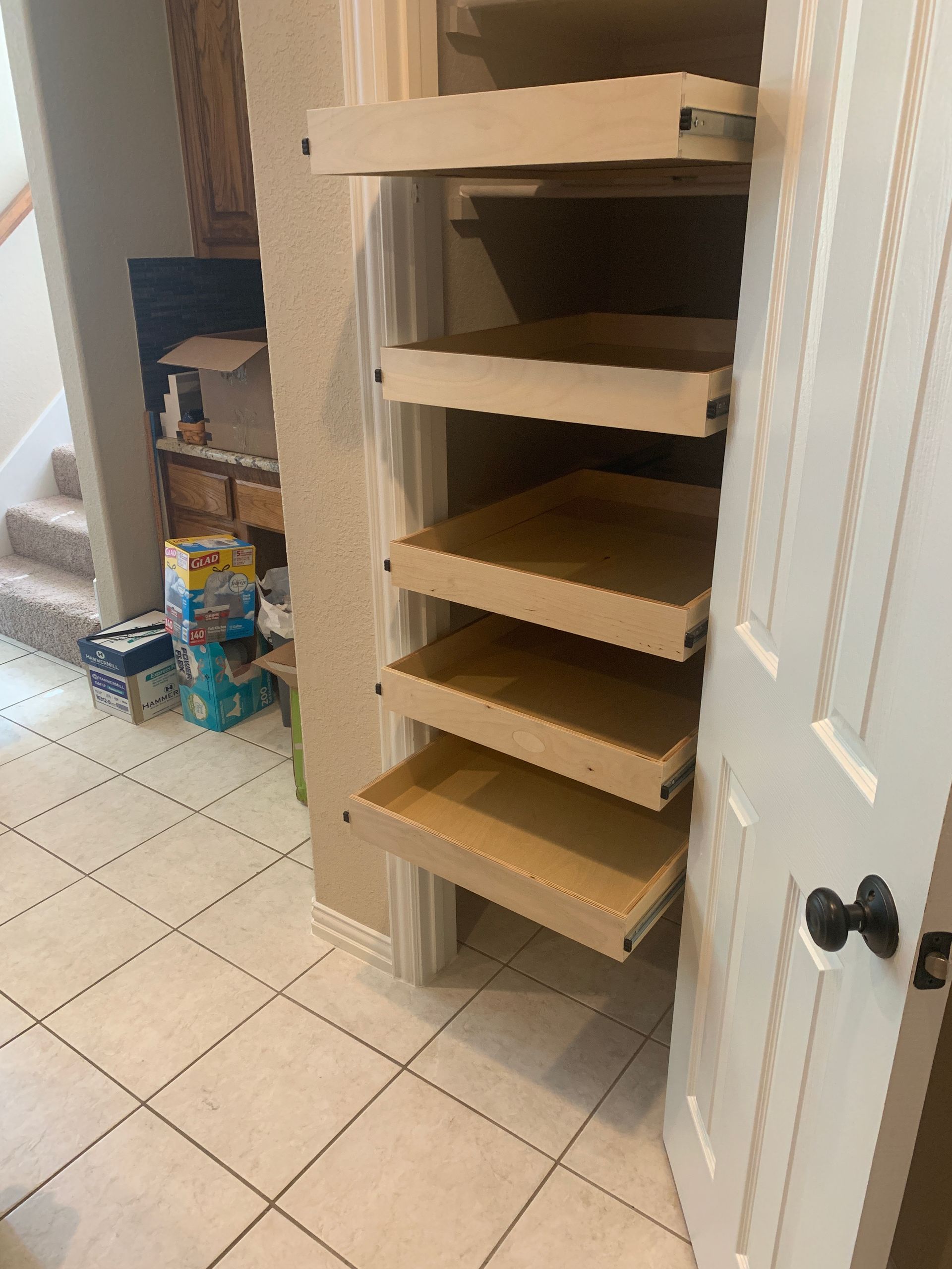 Open pantry with pull-out shelves. Beige shelves contrast with white door and tiled floor.