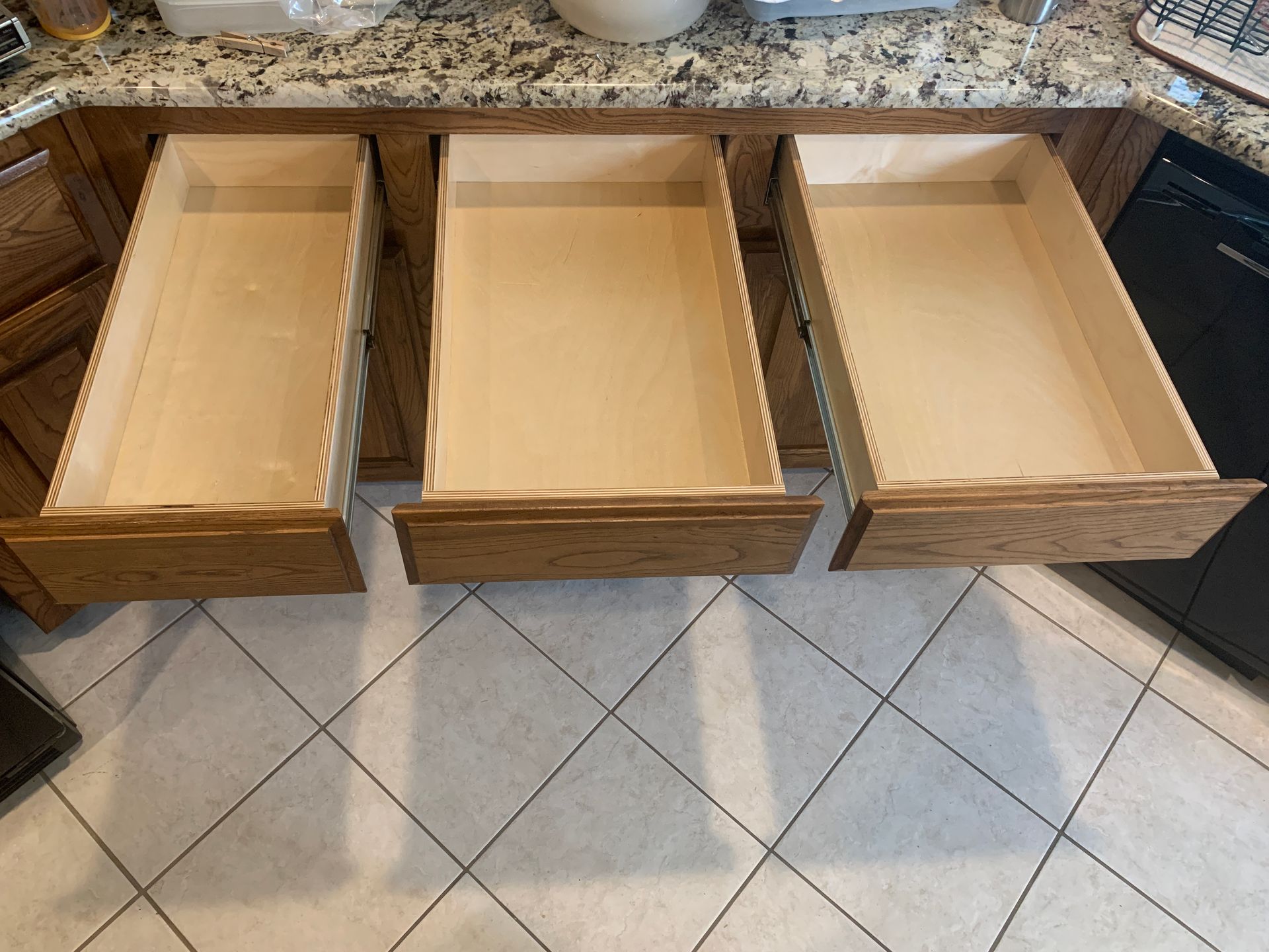 Three open kitchen drawers, wooden construction. Drawer fronts are medium brown, interior light beige.
