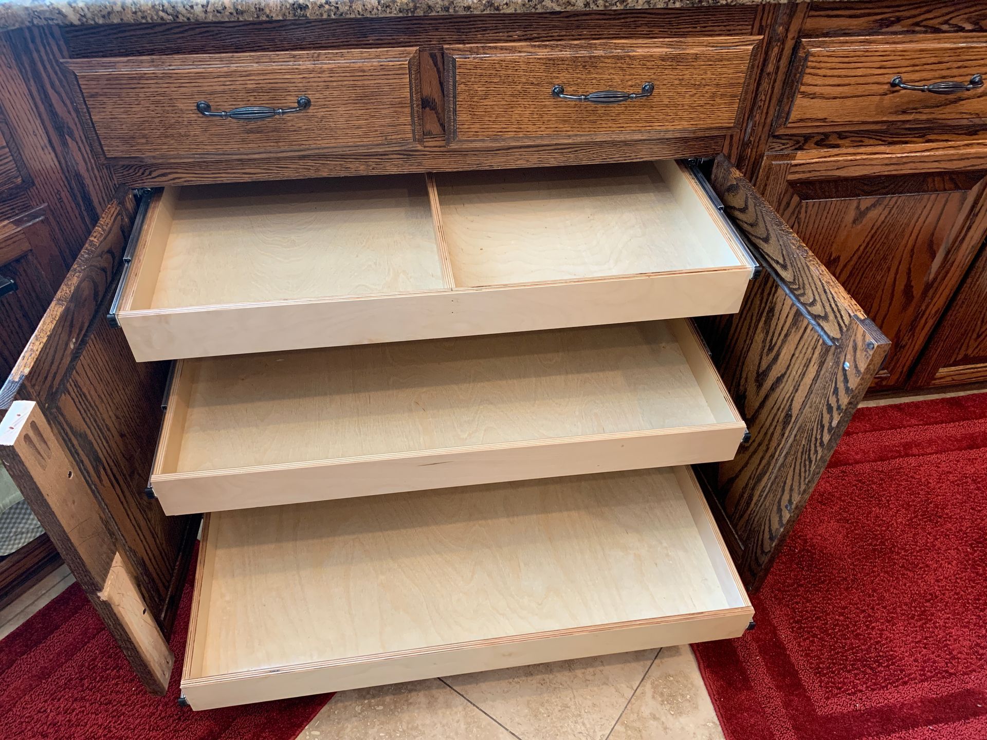 Wooden kitchen cabinet with three pull-out shelves, open. Beige interiors, brown exterior.